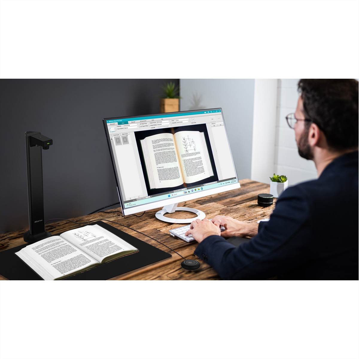 Homme tape sur PC, scanner de livre et livre ouvert sur un bureau.