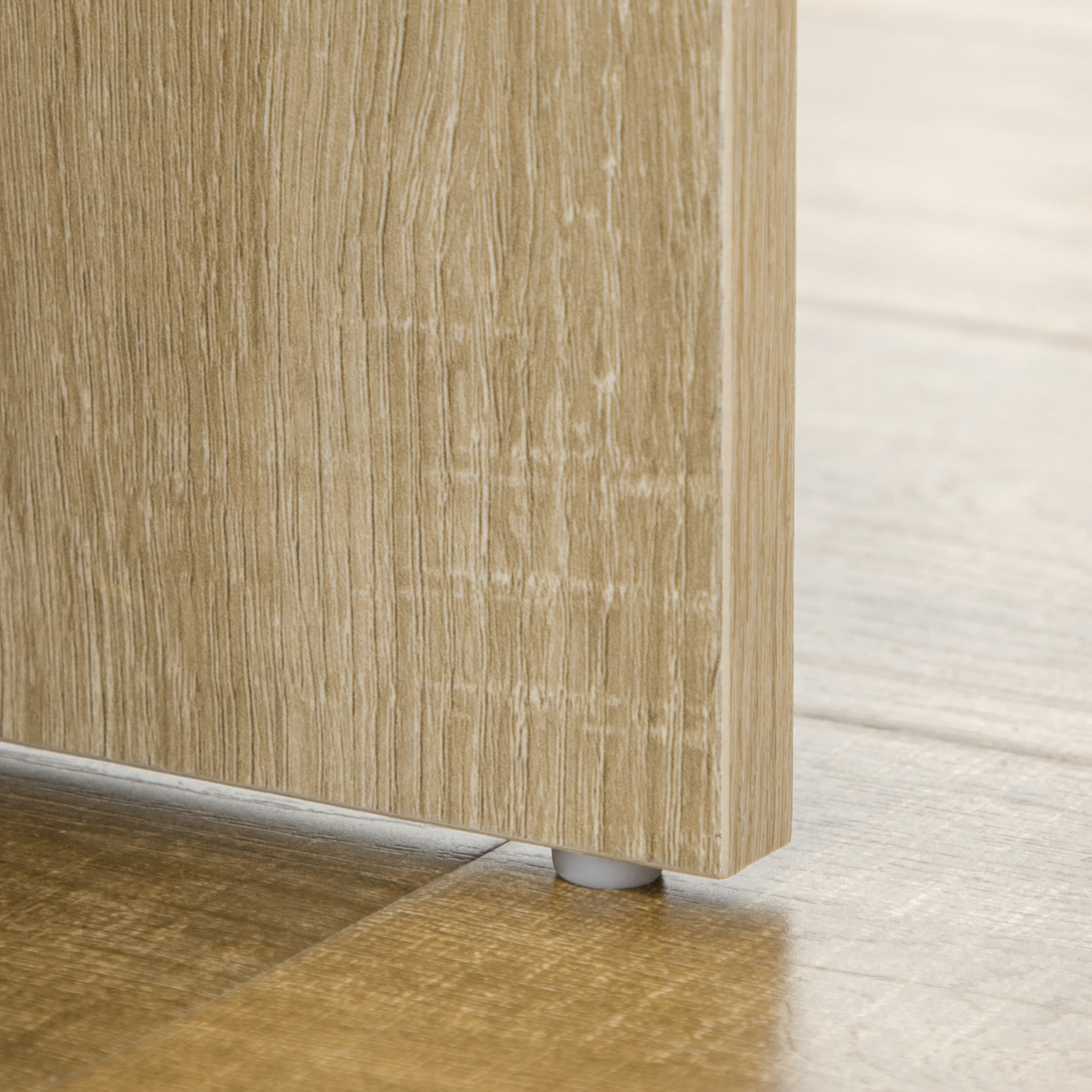Una gamba di mobile in legno con proteggi-pavimento bianco poggia su un pavimento in legno.