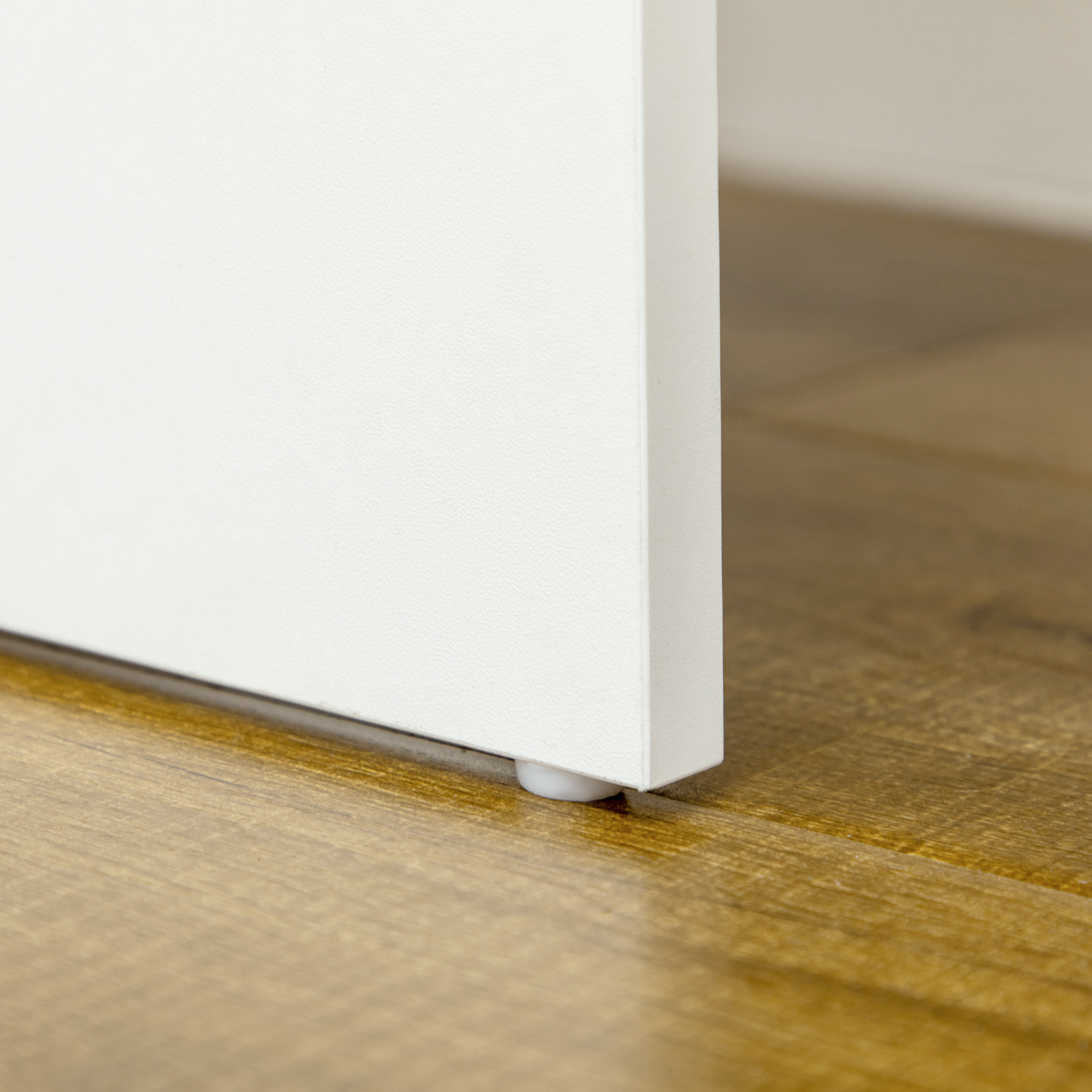 Un mobile bianco si trova su un pavimento in legno, con un piedino bianco visibile.