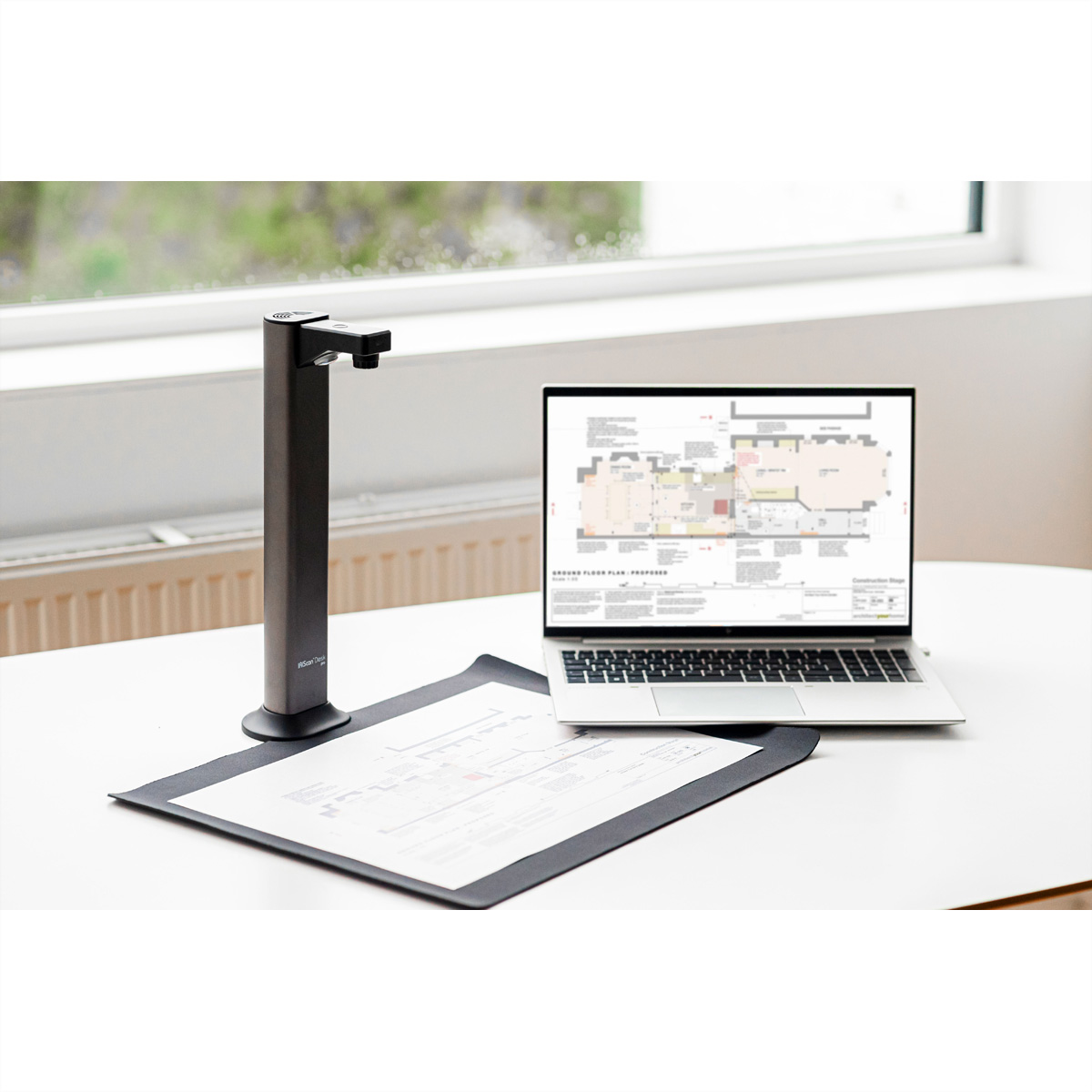 Un scanner de documents se trouve à côté d'un ordinateur portable affichant un plan sur une table blanche.