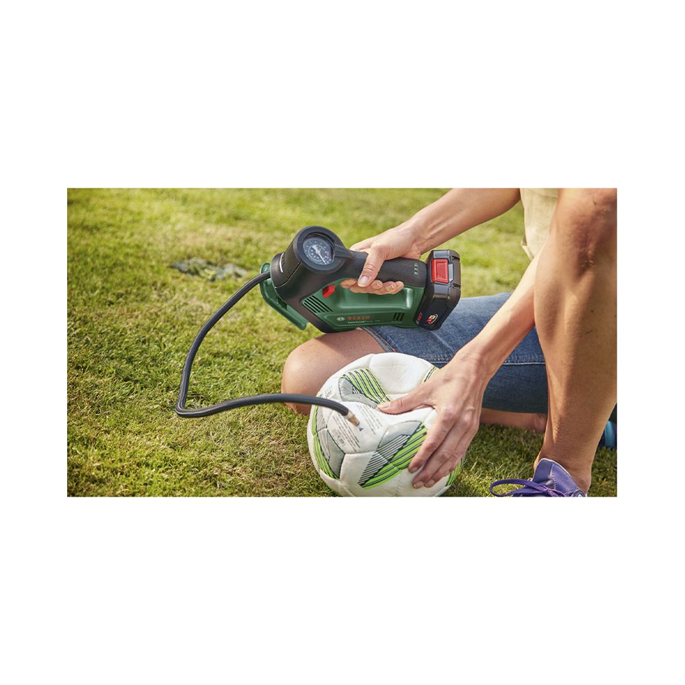 Persona che gonfia un pallone da calcio sull'erba con una pompa ad aria verde.