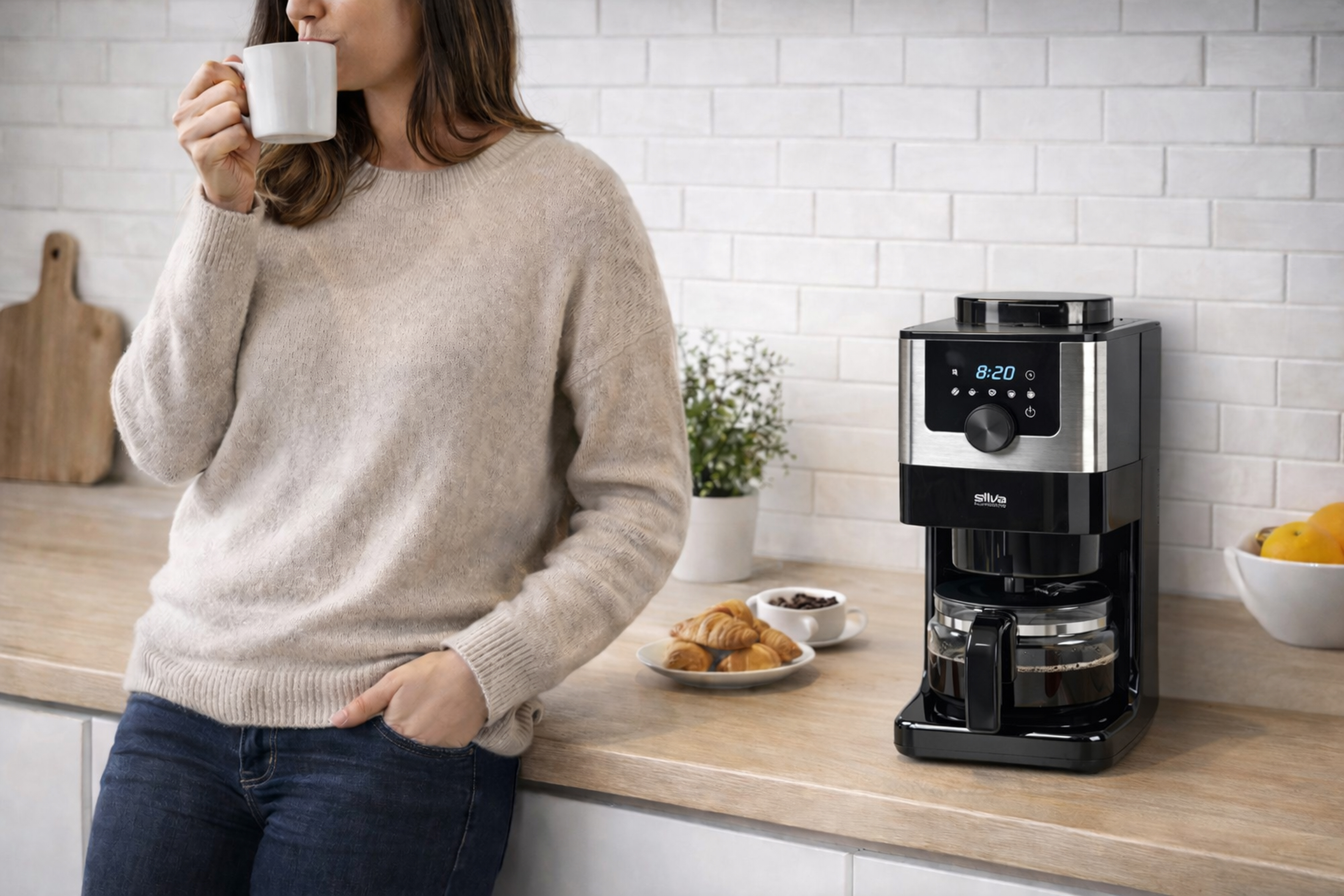 Eine Frau trinkt Kaffee neben einer Kaffeemaschine mit Croissants und Obst.