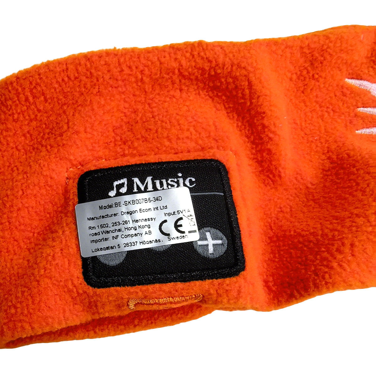 Ein orangefarbenes Fleece-Stirnband mit einem schwarzen Etikett, das Musik und Produktinformationen anzeigt.