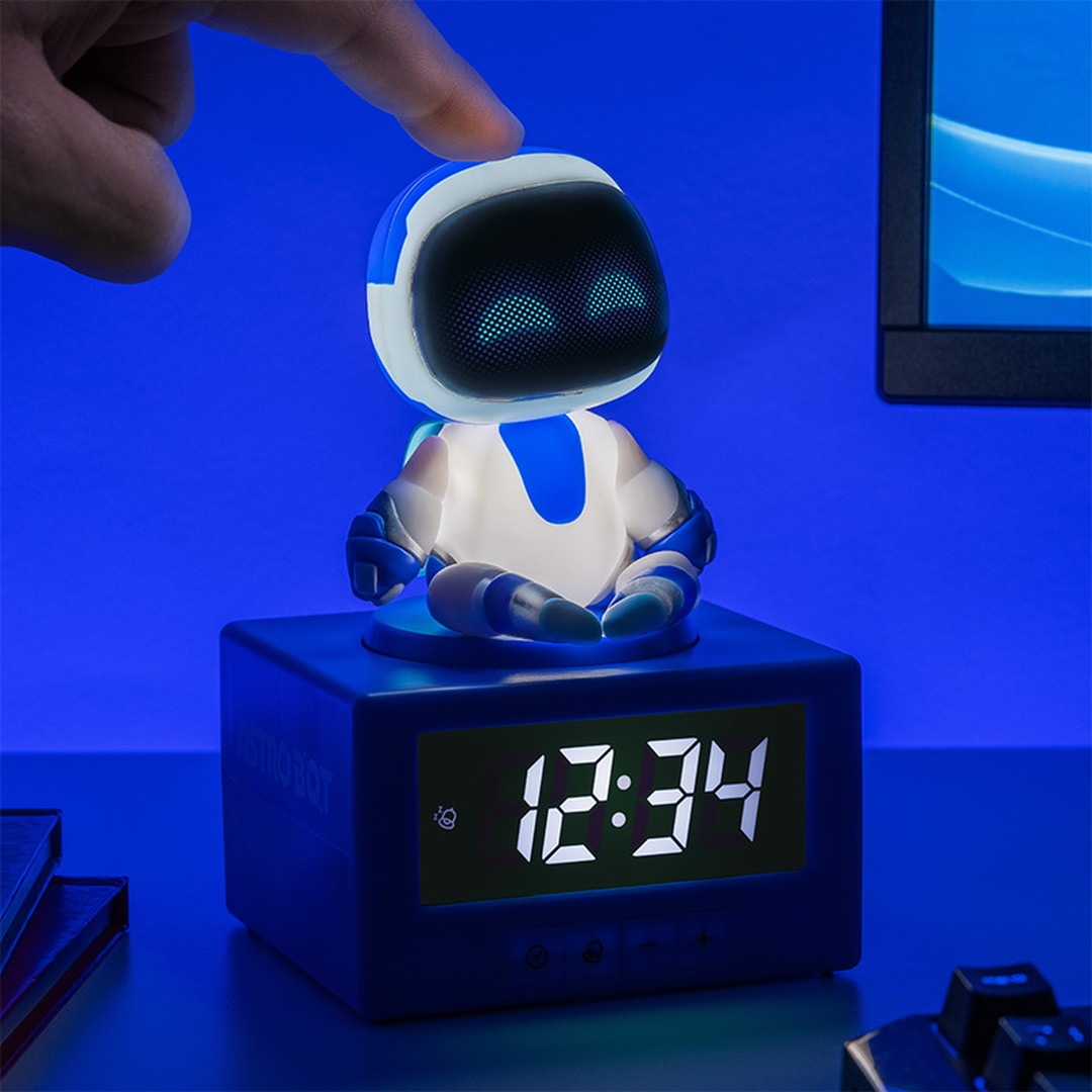 Niebieski robot siedzi na zegarze cyfrowym wyświetlającym 12:34. Palec dotyka jego głowy.