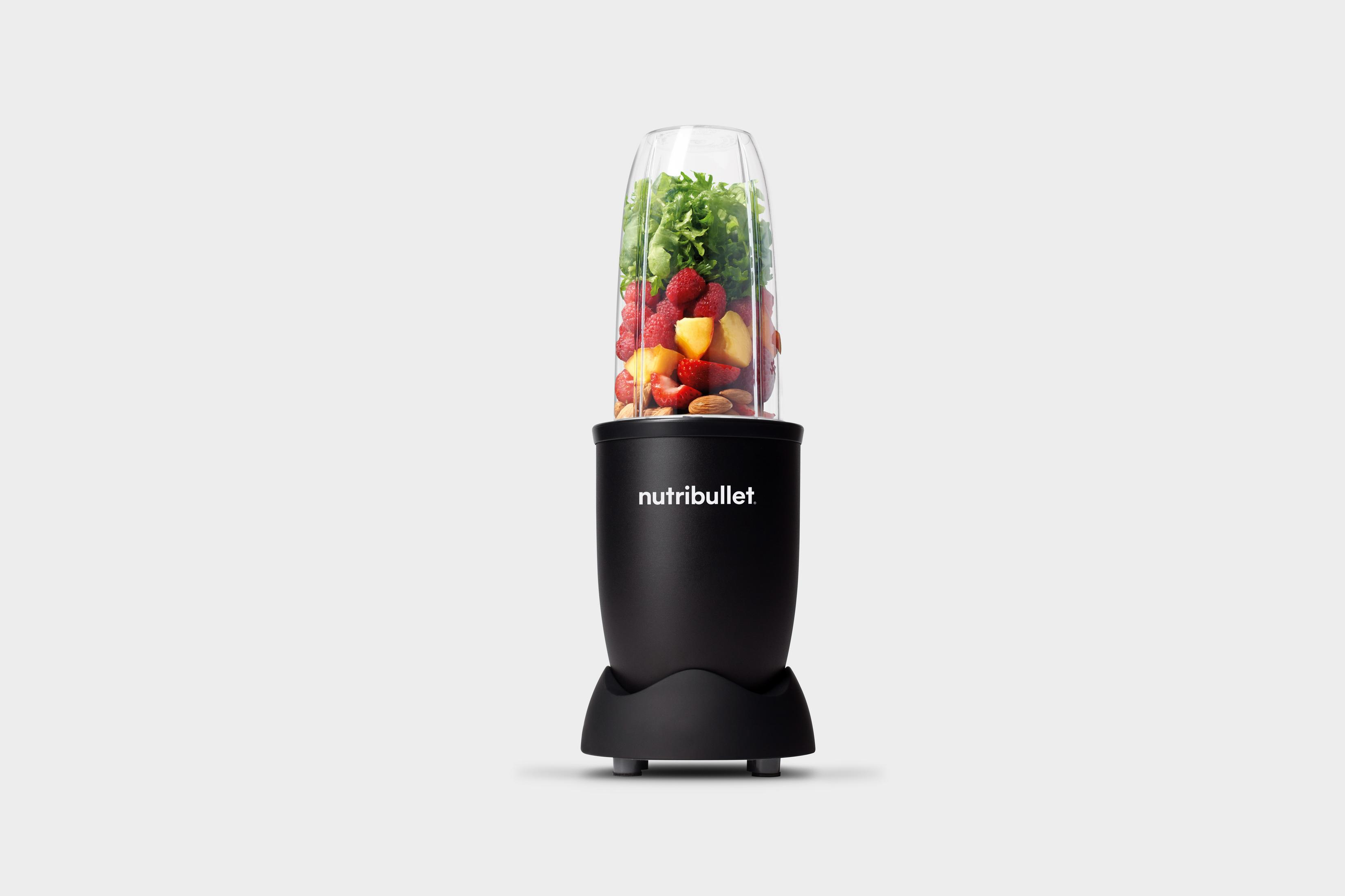 Una licuadora Nutribullet negra con frutas y verduras en el vaso transparente.