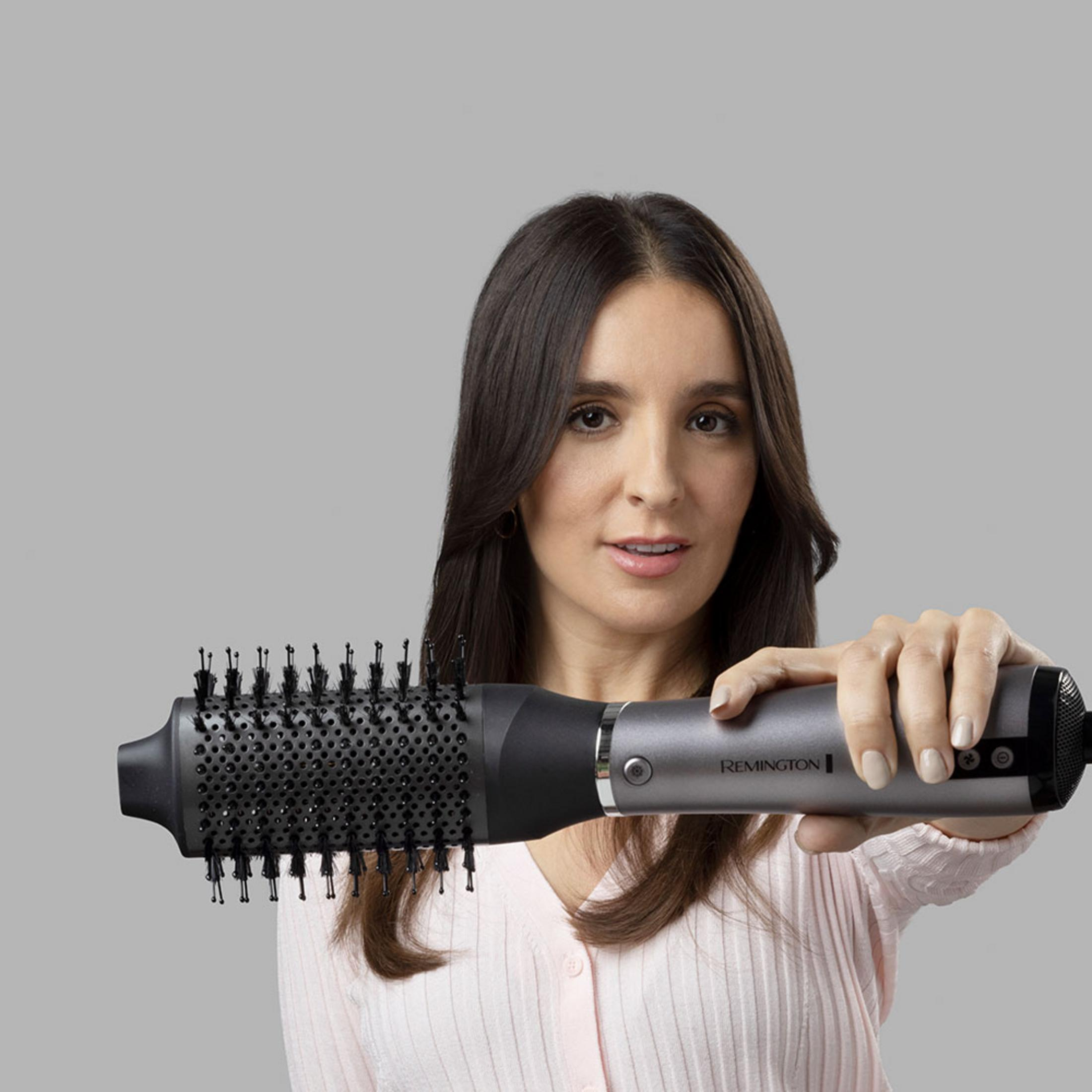 Donna con capelli castani tiene un asciugacapelli Remington argentato con spazzola tonda.