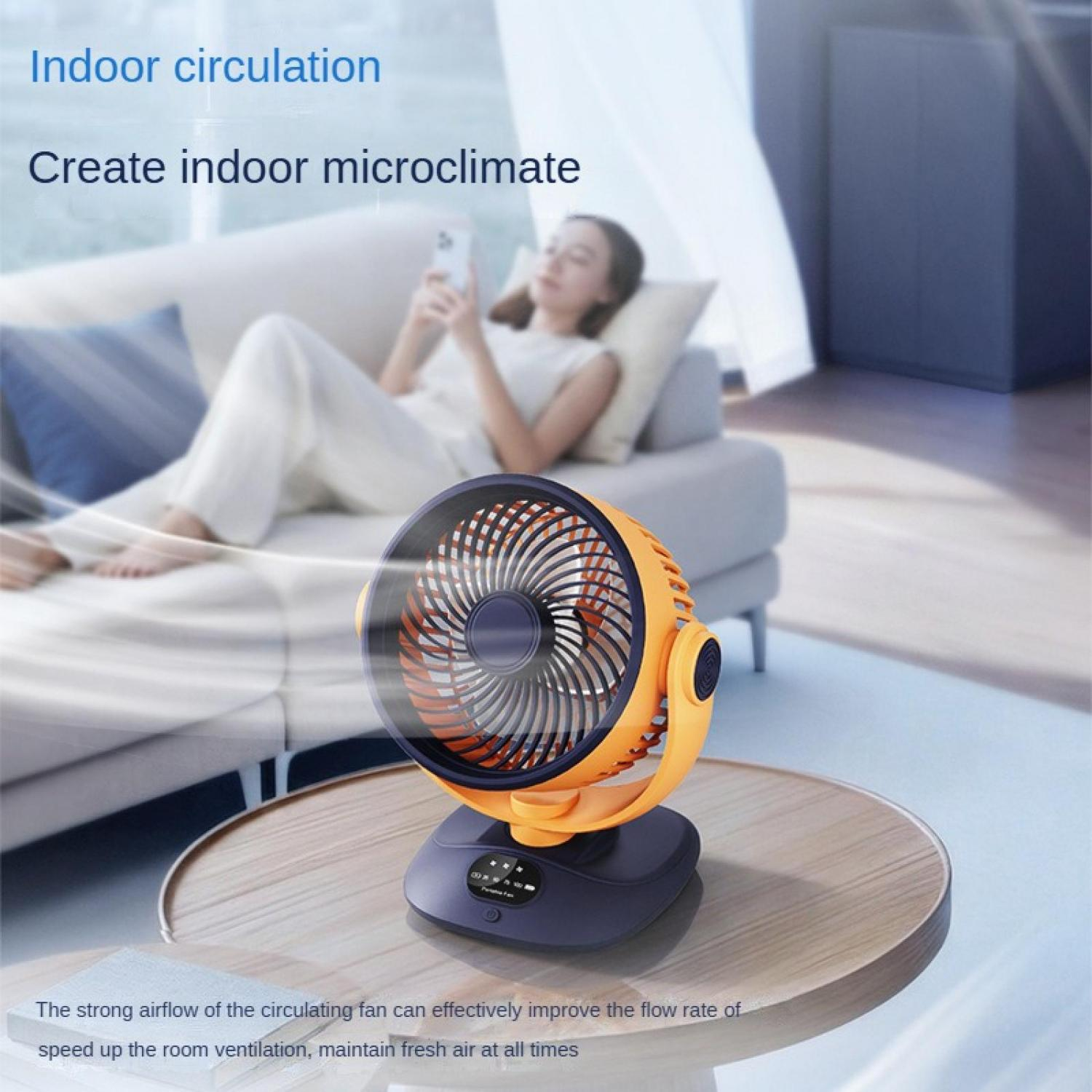 Ein orangefarbener Ventilator steht auf einem Holztisch, im Hintergrund eine Frau auf einem Sofa.