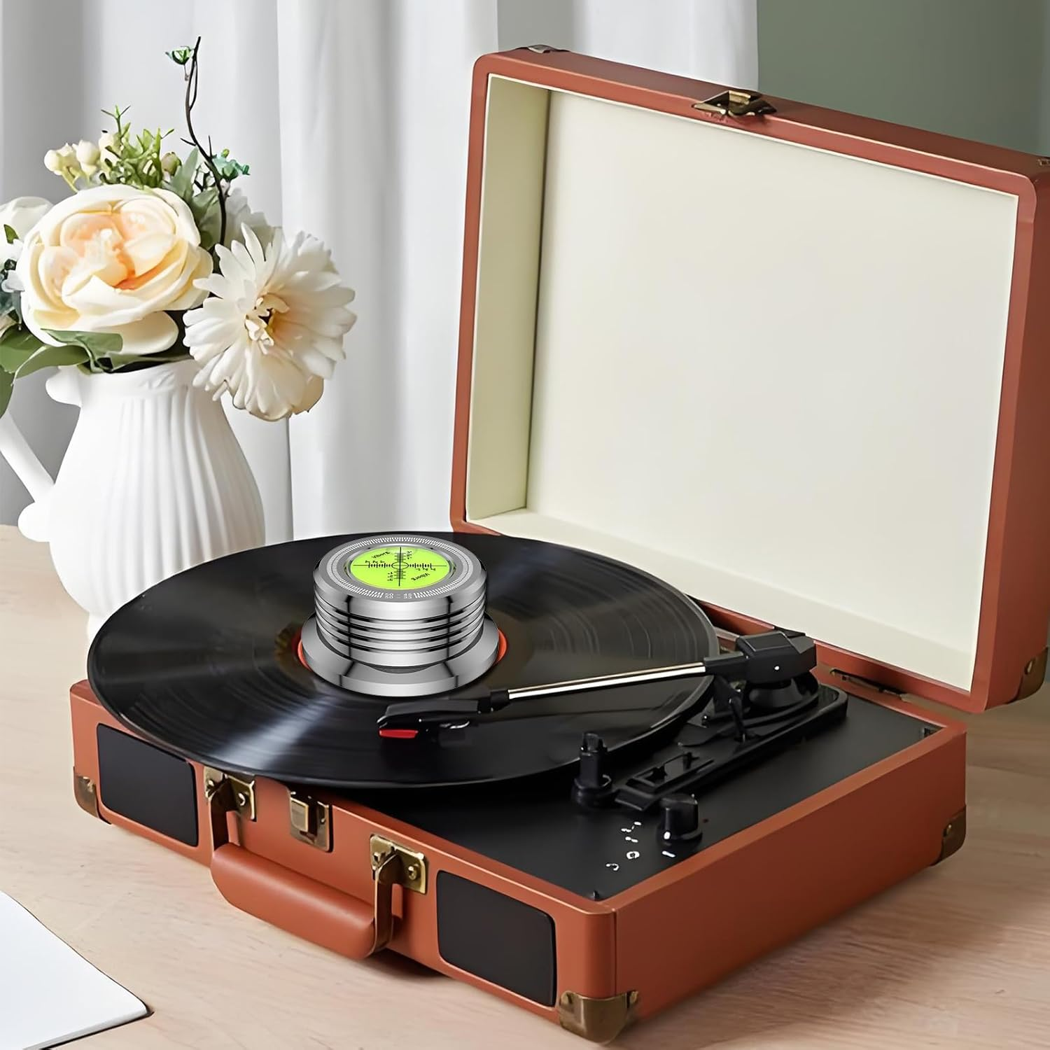 Brauner Plattenspieler mit schwarzer Vinyl-Schallplatte, silberner Messuhr und Blumenvasen.