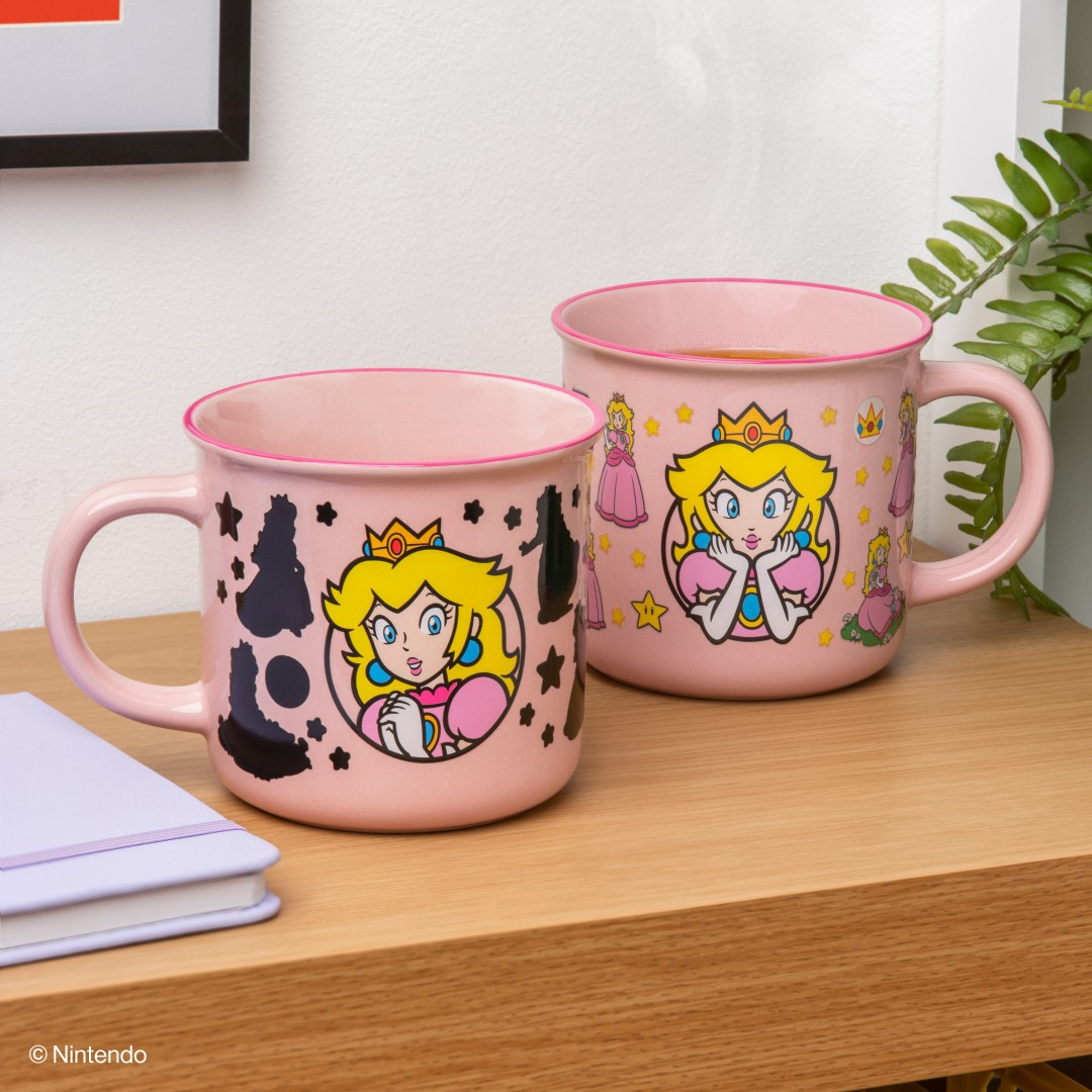 Dwa różowe kubki z motywami Księżniczki Peach, jeden z czarnymi sylwetkami, jeden napełniony.