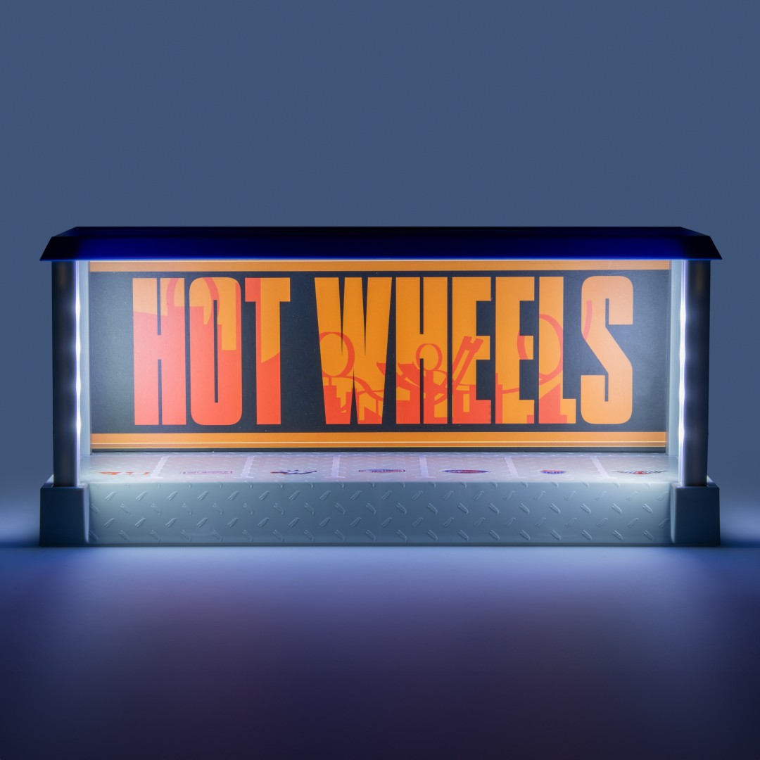 Podświetlany znak "HOT WHEELS" z pomarańczowym tekstem na czarnym tle.