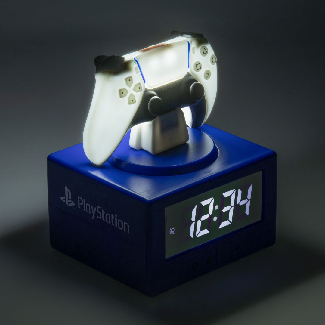 Świecący kontroler PlayStation na niebieskim budziku pokazującym 12:34.