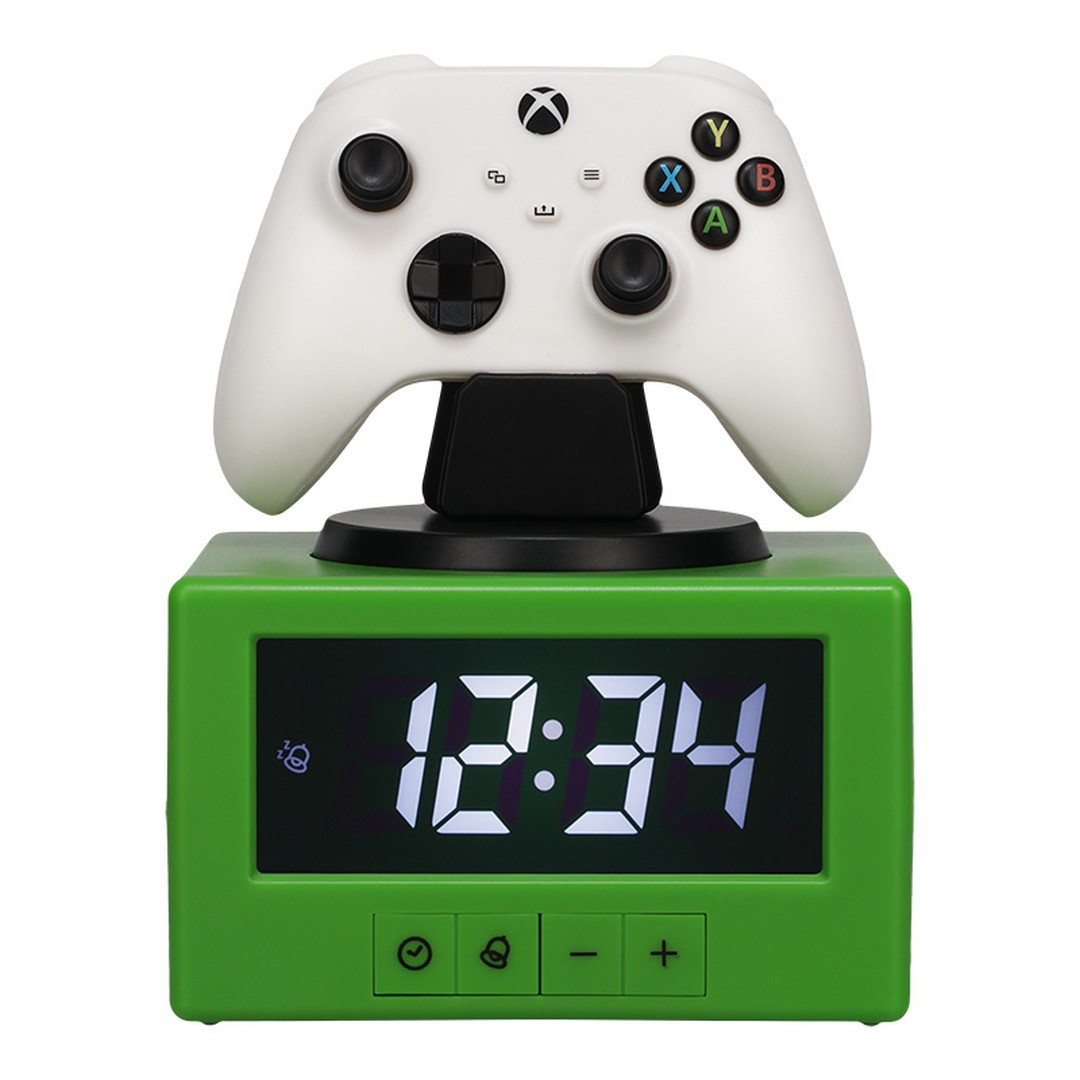 Biały kontroler Xbox stoi na zielonym budziku cyfrowym pokazującym 12:34.