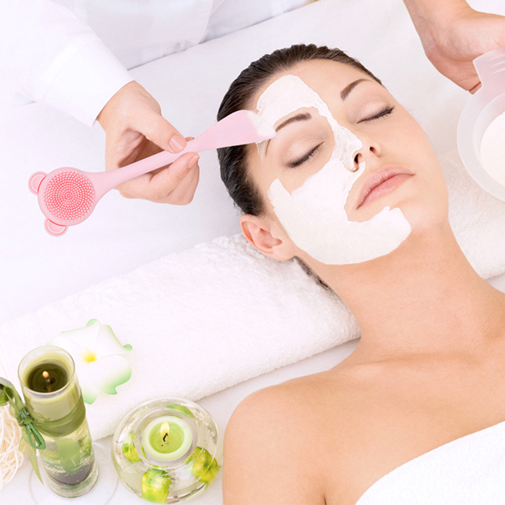 Spa-Szene: Frau mit Gesichtsmaske, trägt Creme mit Pinsel auf. Kerzen, Blume.