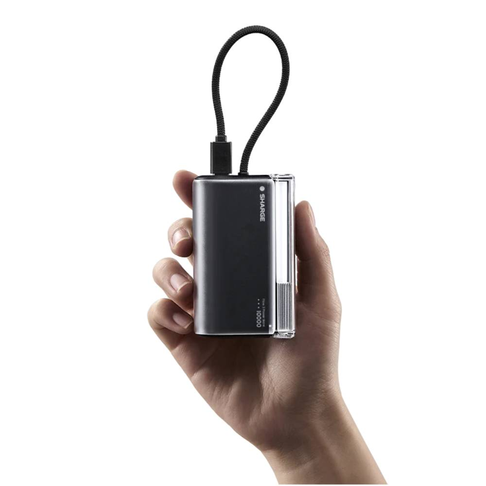 Batterie externe grise avec câble noir tenue dans une main sur fond blanc.