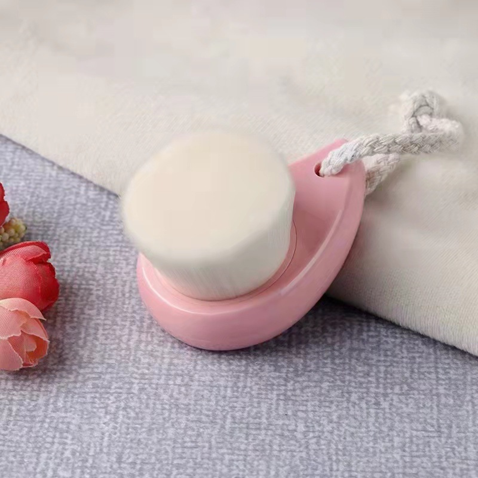 Rosa Gesichtsreinigungsbürste mit weißen Borsten auf strukturierter Oberfläche.