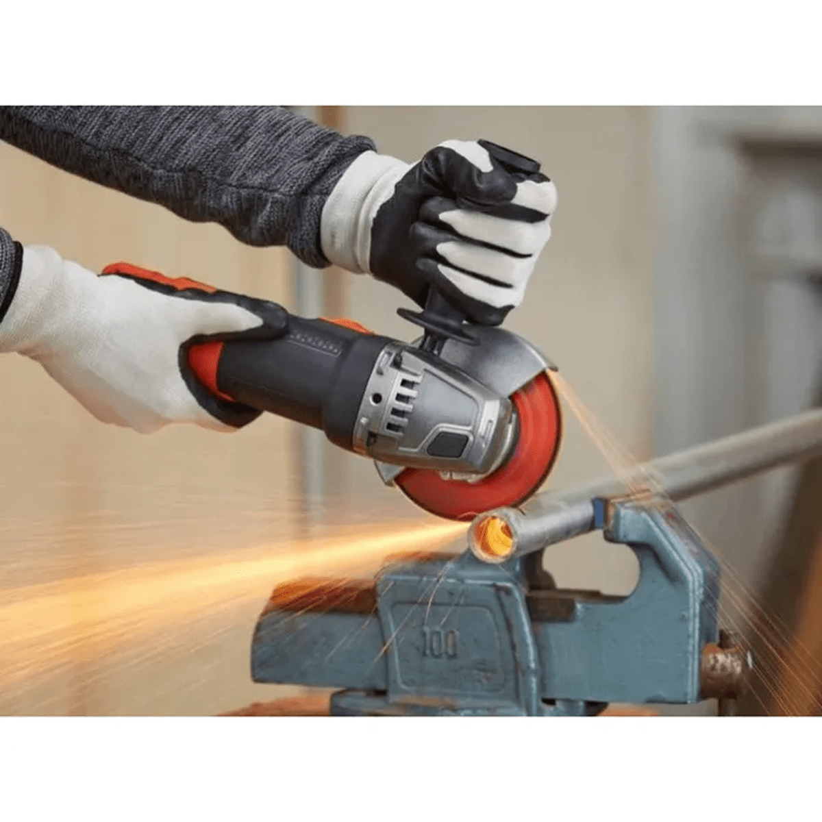 Ein Mann mit Handschuhen schneidet mit einem Winkelschleifer ein Rohr, das in einem Schraubstock eingespannt ist.