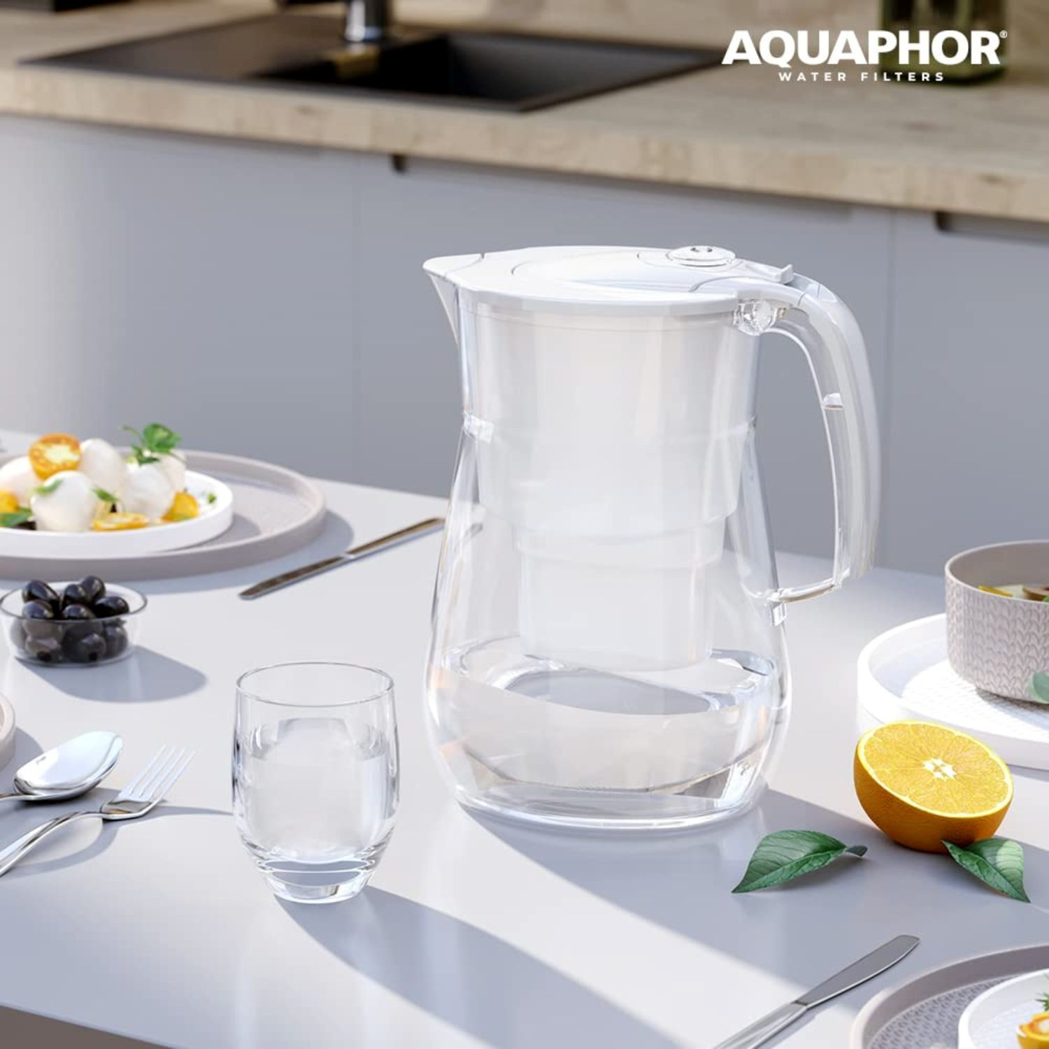 Ein Aquaphor-Wasserfilterkrug steht auf einem Tisch neben einem Glas Wasser und Obst.
