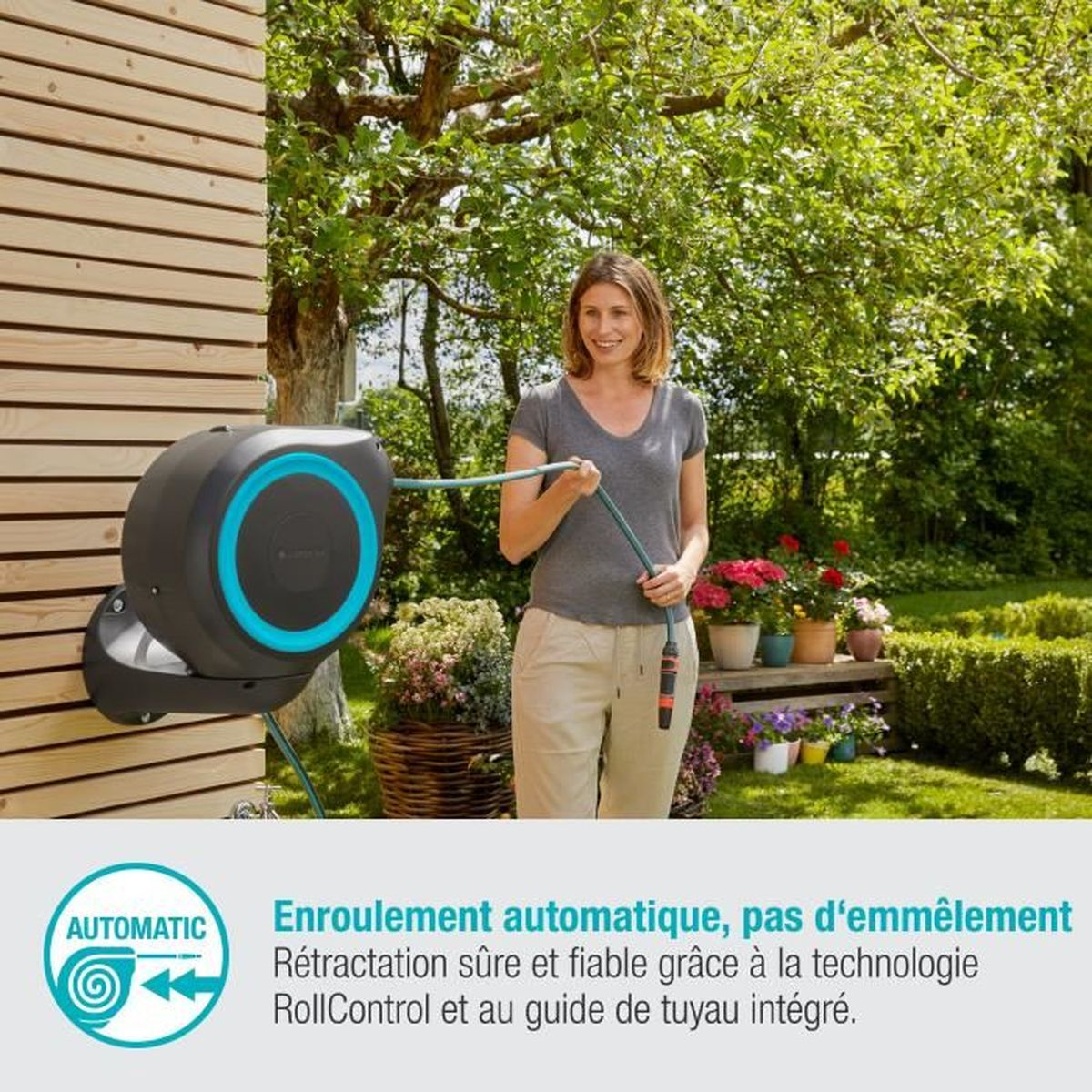 Donna tiene tubo da giardino accanto a avvolgitubo automatico su parete in legno.