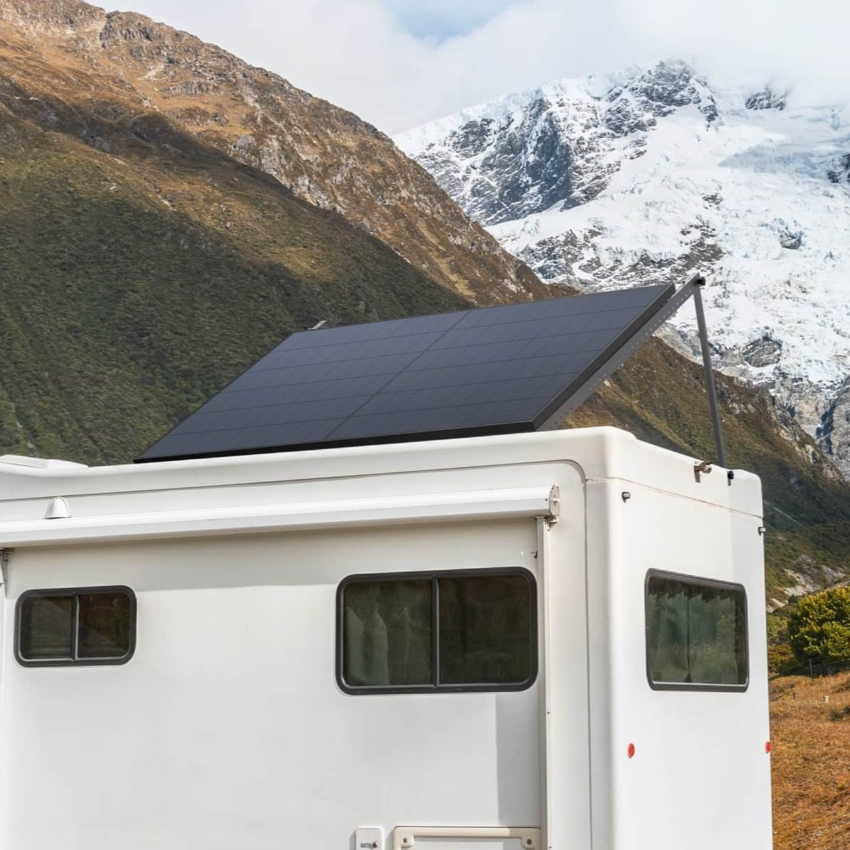 Un camper con pannelli solari sul tetto è parcheggiato di fronte a un paesaggio montano innevato.