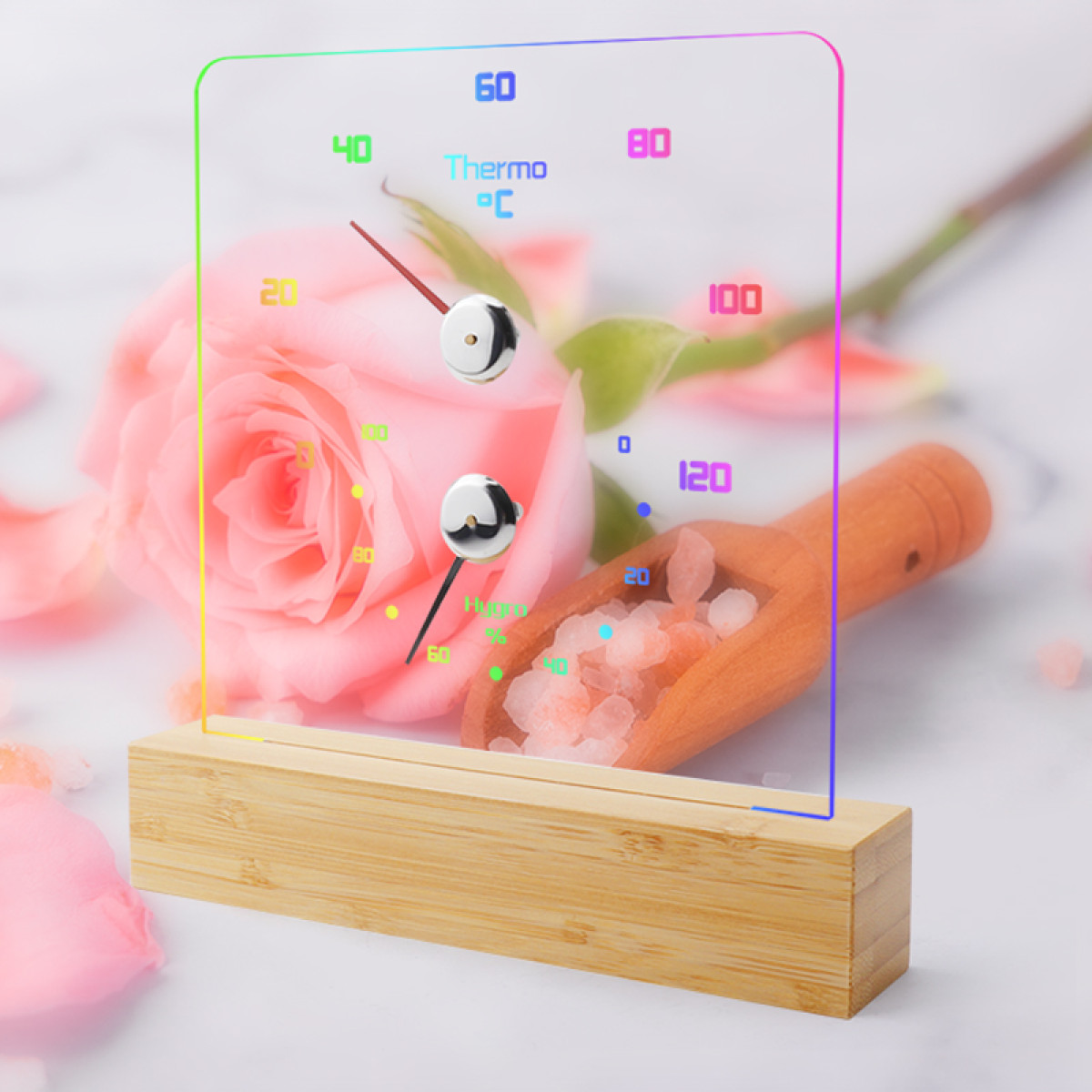 Ein digitaler Thermometer/Hygrometer mit bunten LED-Rändern auf einem Holzsockel.