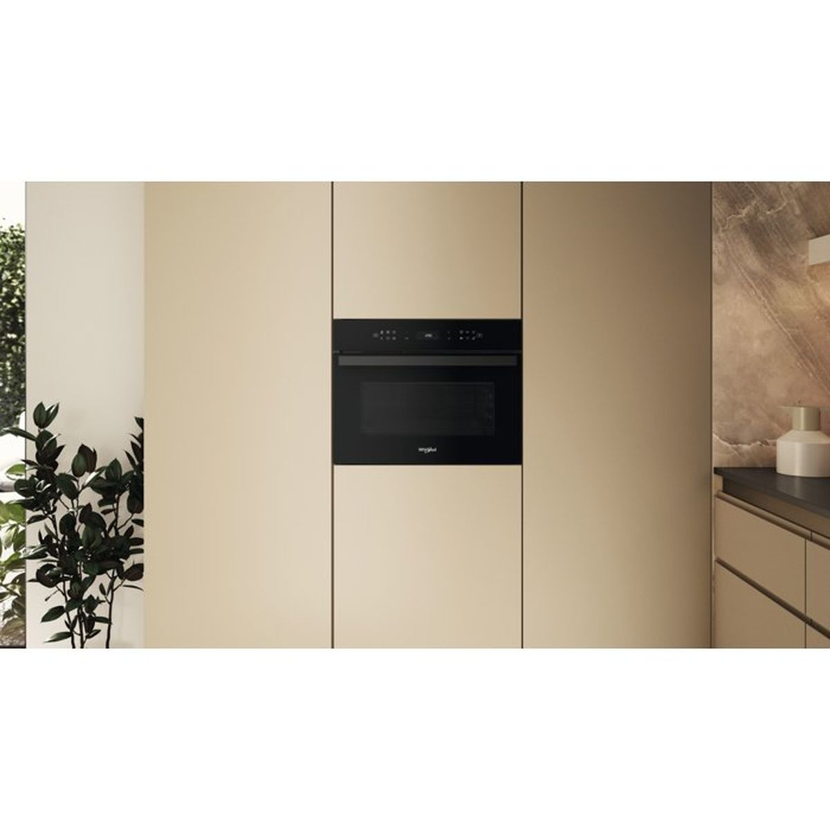 Einbau-Mikrowelle in einem modernen Küchenschrank in Beige, daneben eine Pflanze.