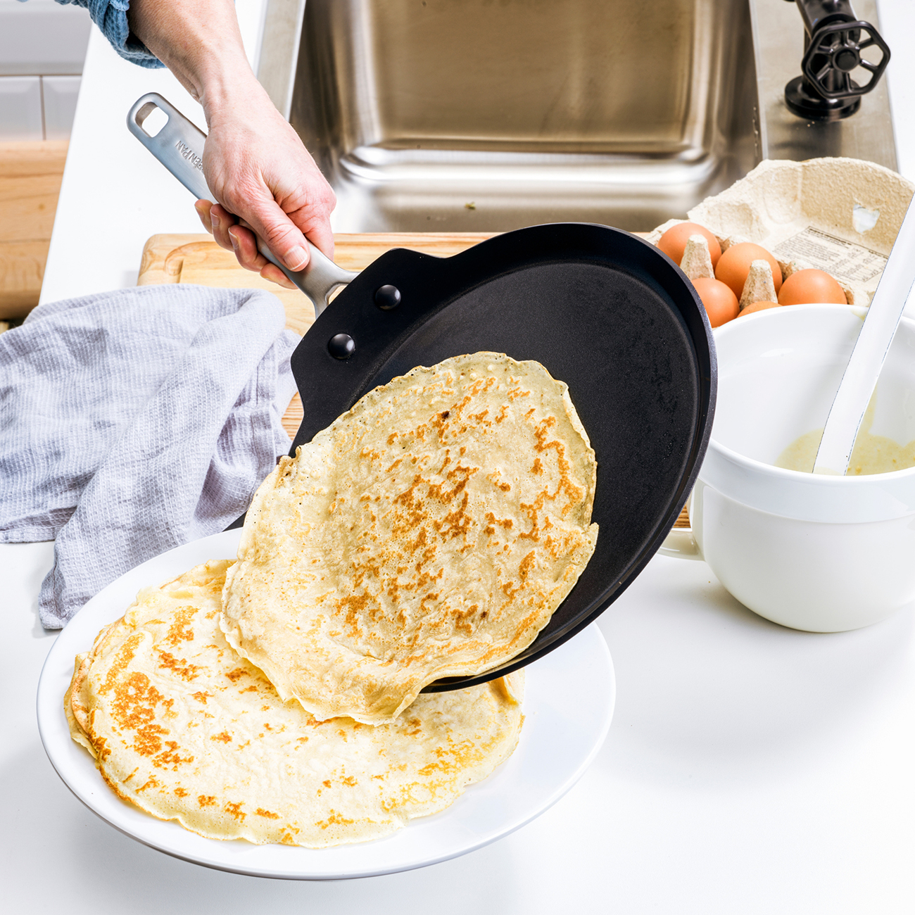 Eine Hand kippt einen Pfannkuchen aus einer Pfanne auf einen Teller mit anderen Pfannkuchen.