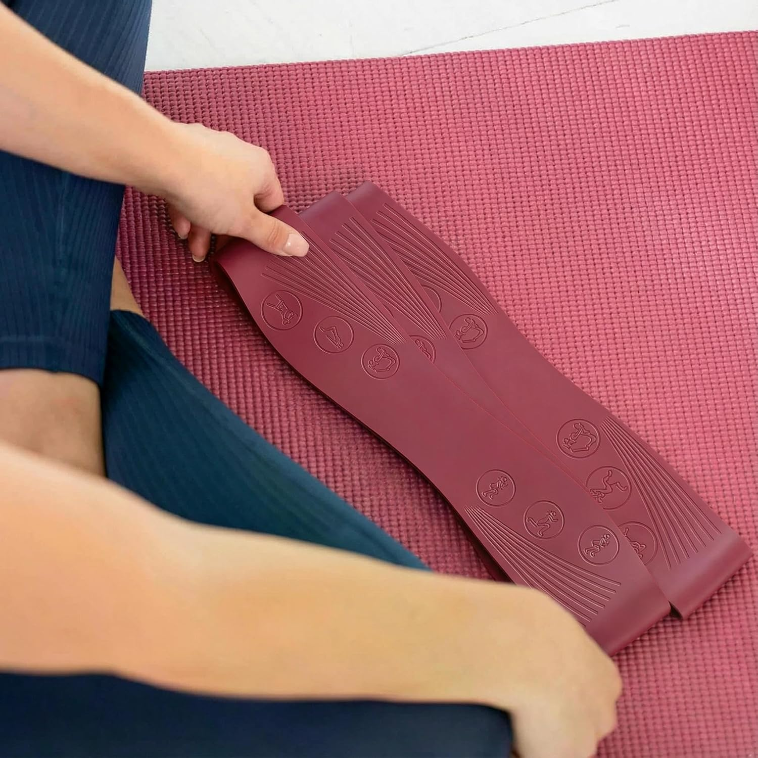 Person in blauer Leggings auf einer kastanienbraunen Yogamatte mit kastanienbraunem Dehnwerkzeug.
