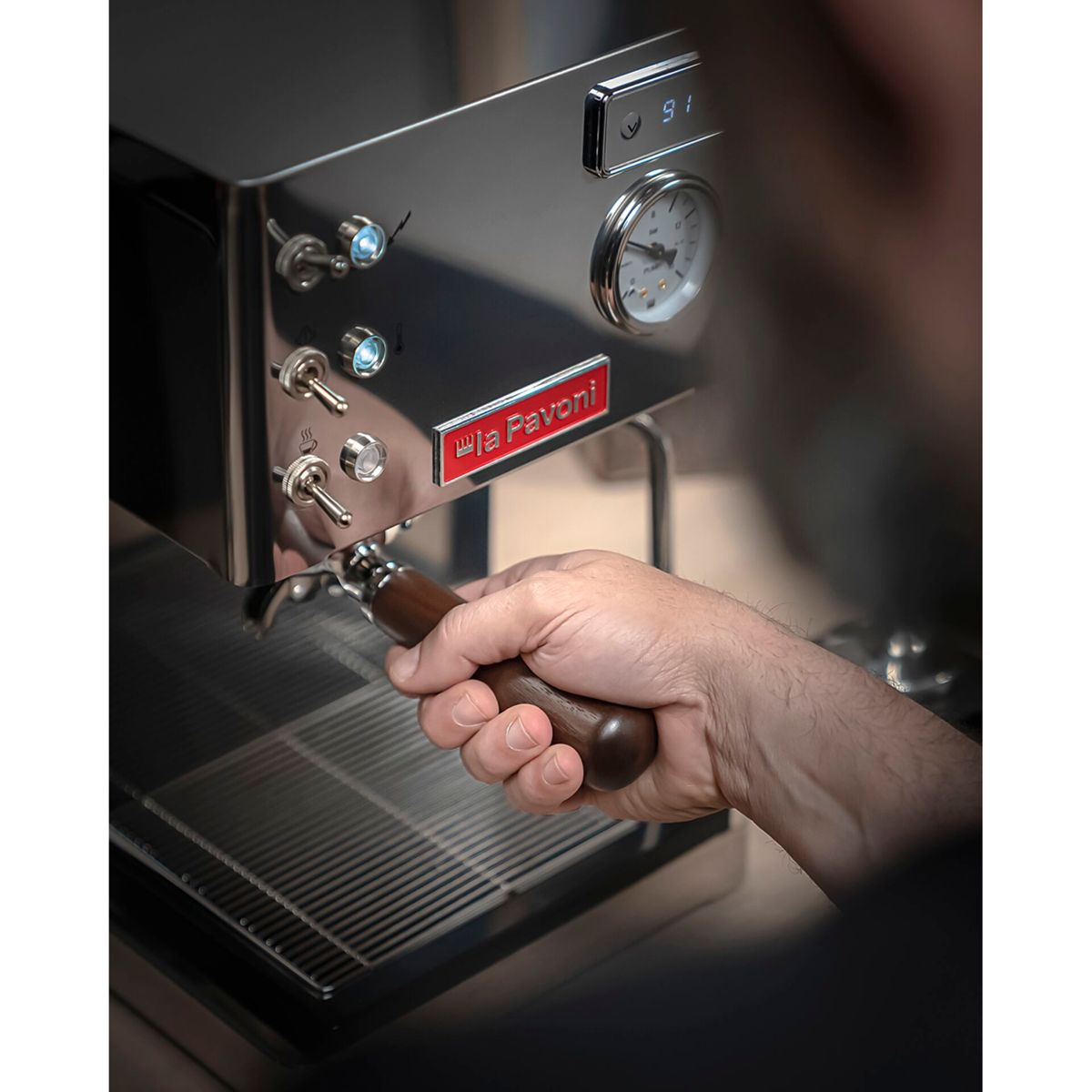 Eine Hand hält einen Holzgriff an einer Espressomaschine mit Manometer.