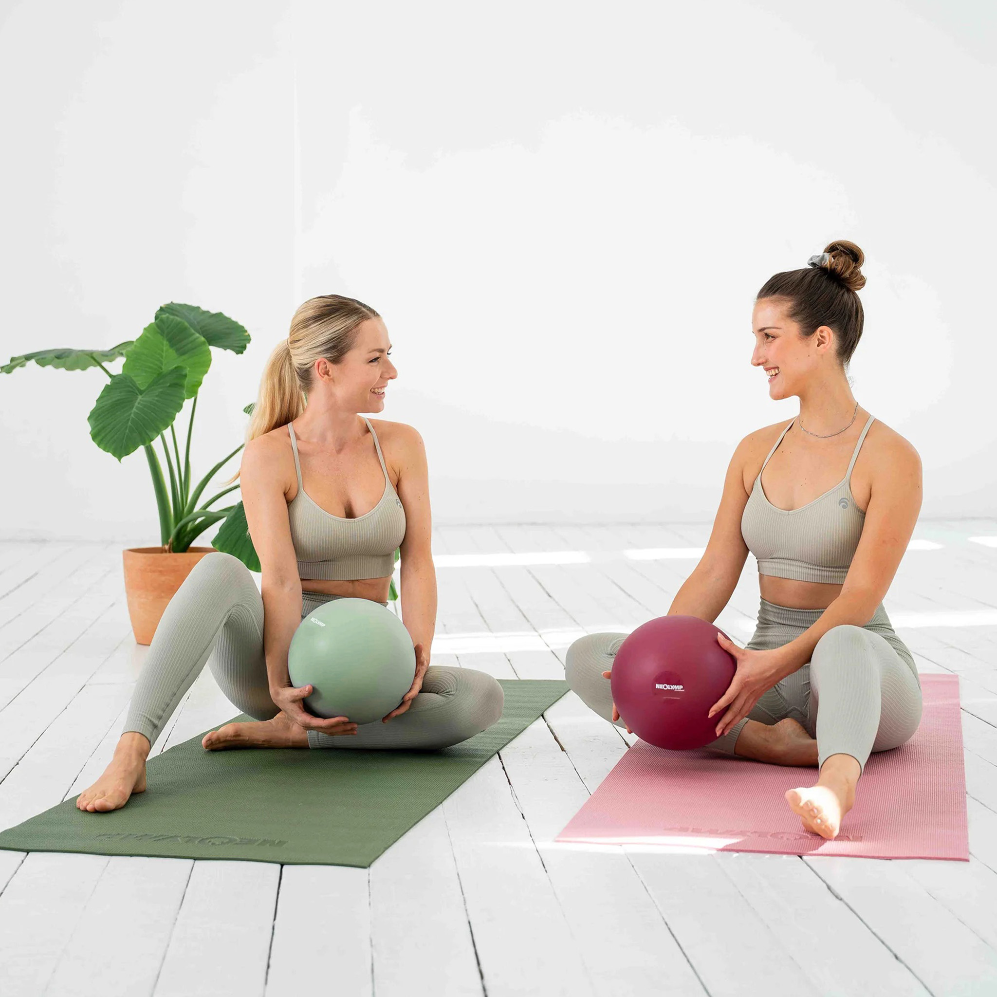 Zwei Frauen sitzen auf Yogamatten und halten Bälle.