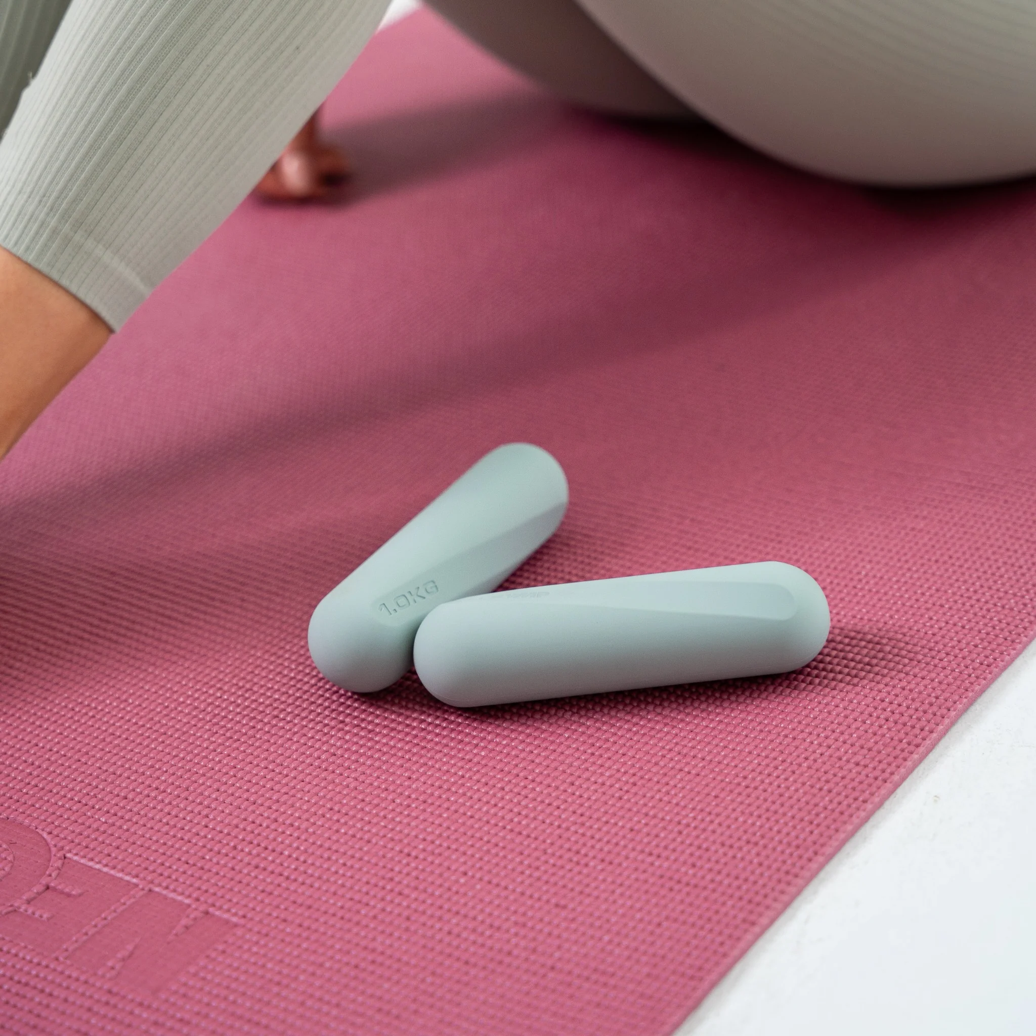 Zwei hellgrüne Hanteln liegen auf einer rosafarbenen Yogamatte.