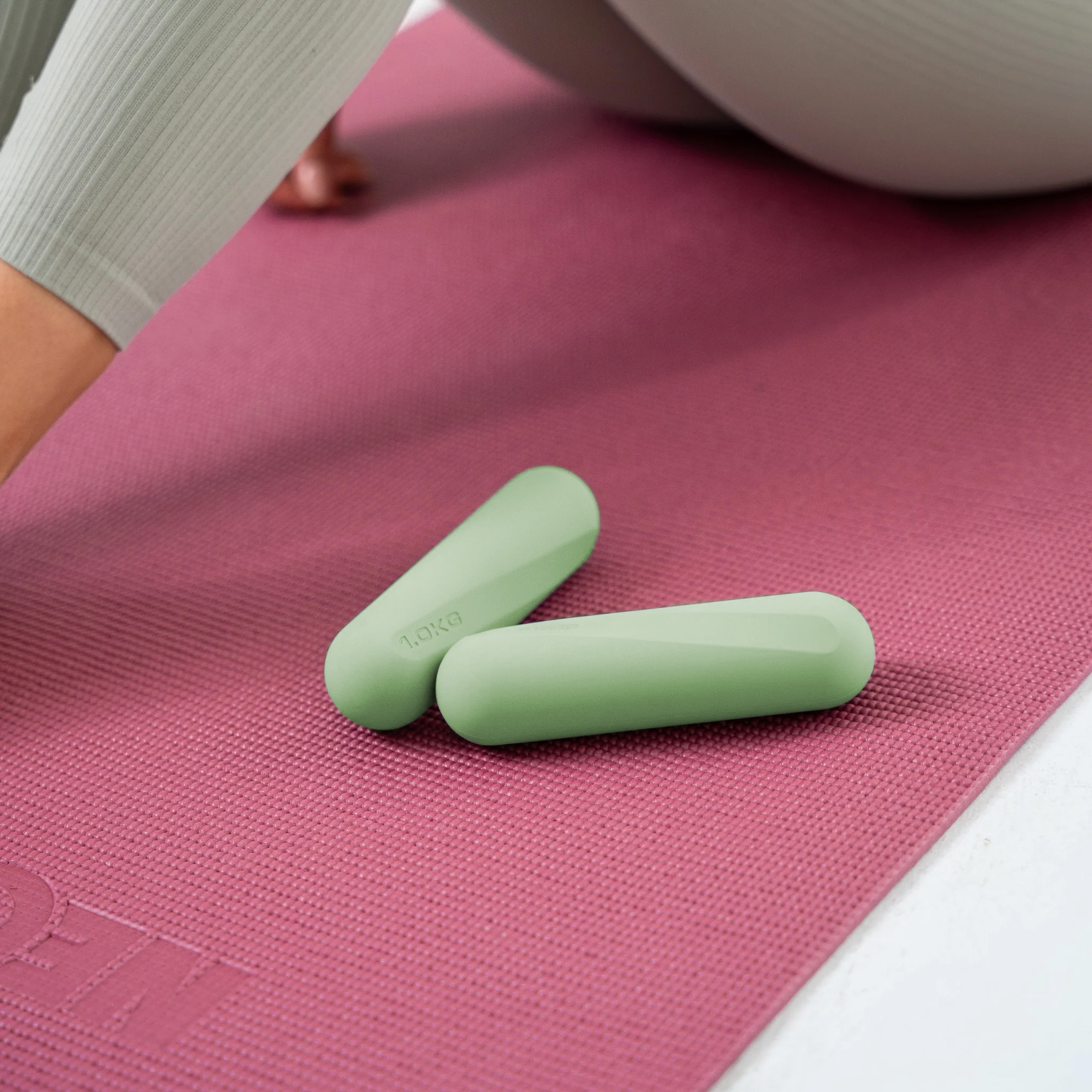 Zwei hellgrüne Hanteln liegen auf einer rötlichen Yogamatte.