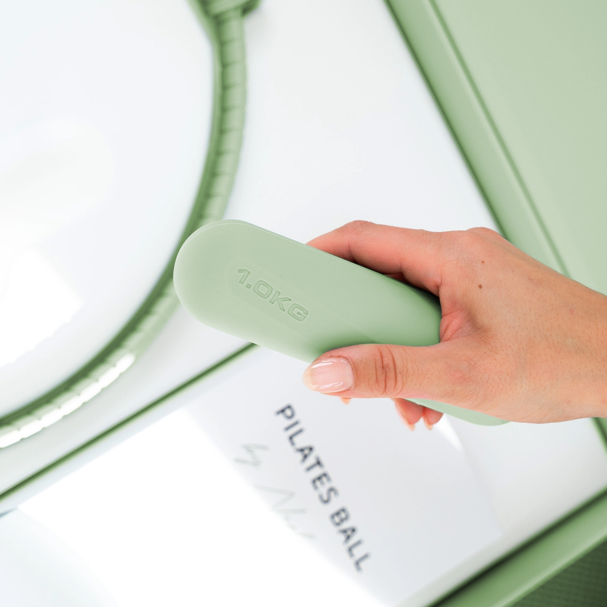 Eine Hand hält einen grünen Pilatesball mit der Aufschrift „1.0KG“.
