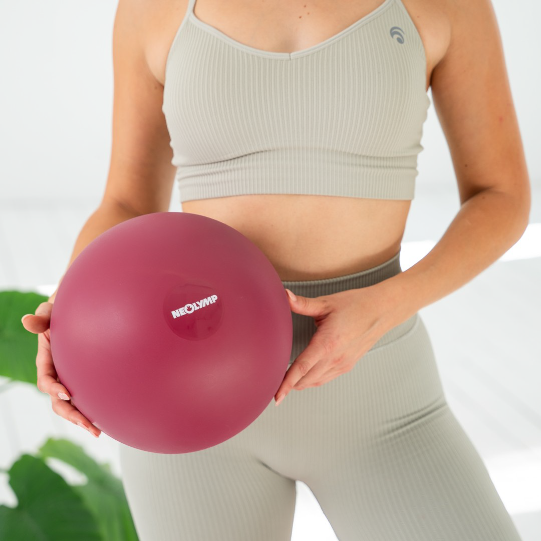 Eine Frau hält einen dunkelroten Gymnastikball mit dem Aufdruck "NEOLYMP".