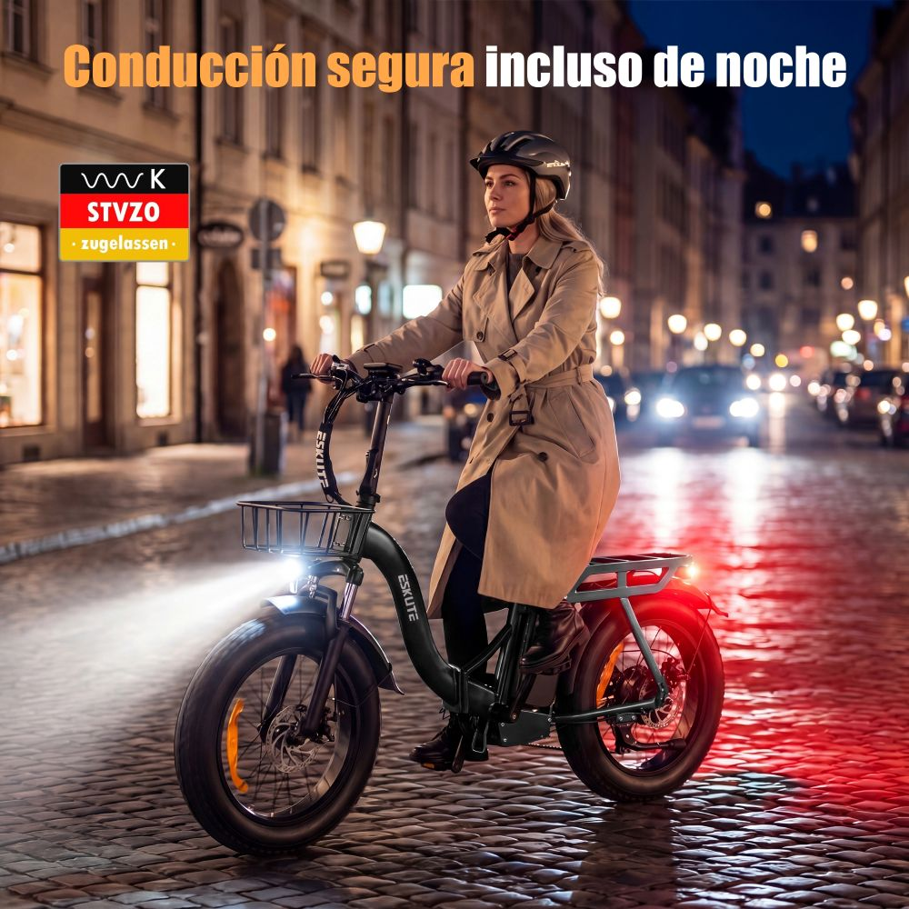 Mujer monta bicicleta eléctrica de noche sobre adoquines; luces encendidas.