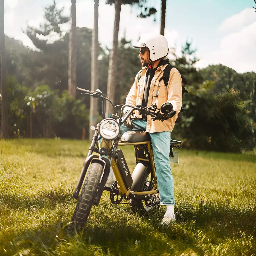 Un hombre con casco se sienta en una e-bike amarilla en la hierba, rodeado de árboles.