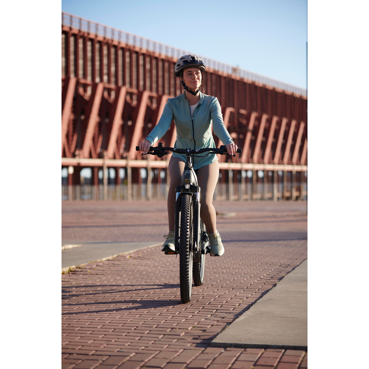 Eine Frau in Sportkleidung fährt mit Helm auf einem Fahrrad auf einem Ziegelweg.