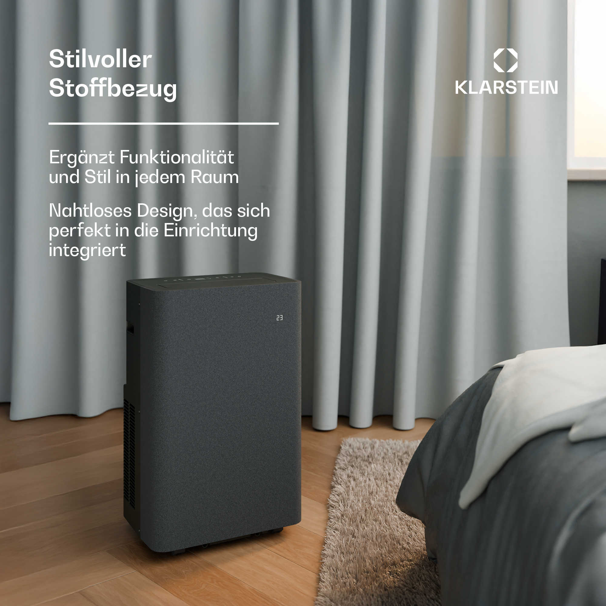 Un condizionatore d'aria scuro con rivestimento in tessuto si trova su un pavimento in legno accanto a un letto.