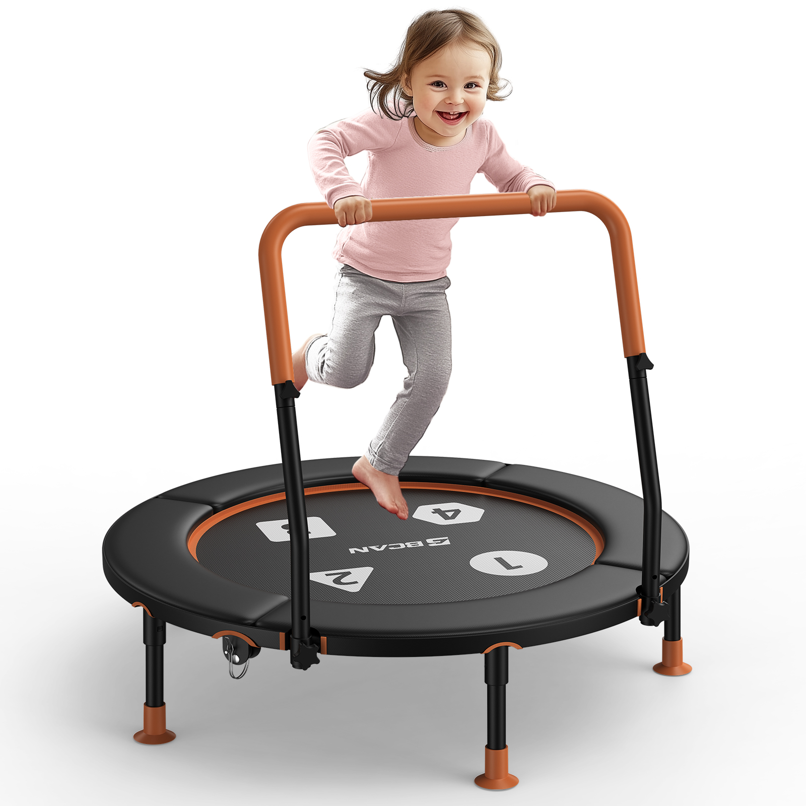 Ein lächelndes Kleinkind in einem rosa Hemd und grauen Hosen springt fröhlich auf einem schwarz-orangen Mini-Trampolin mit Sicherheitsstange.