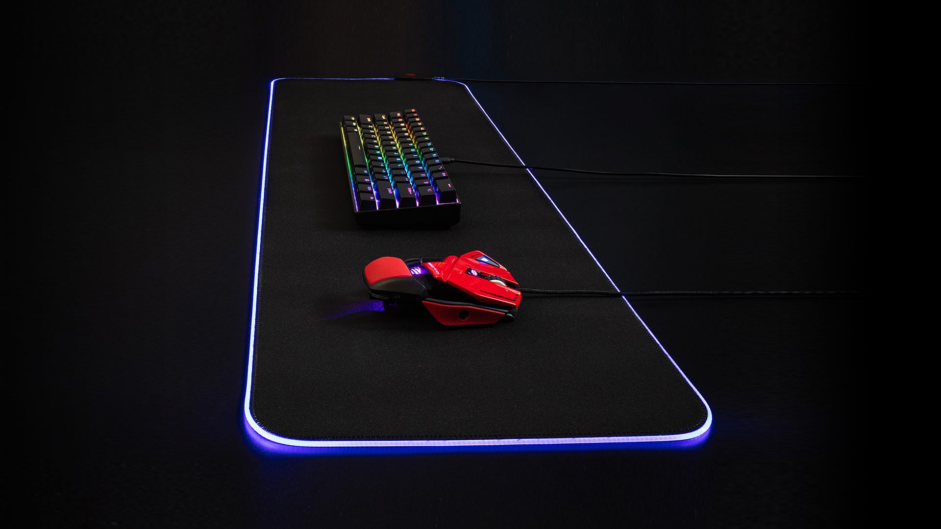 Une souris gaming rouge et un clavier coloré sur un tapis de souris noir avec éclairage RVB.