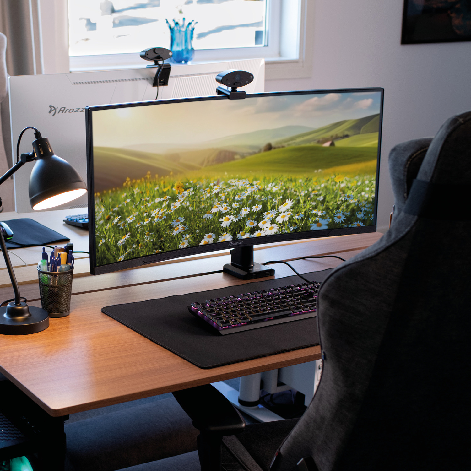 Scrivania con monitor che mostra paesaggio, tastiera, lampada e sedia.