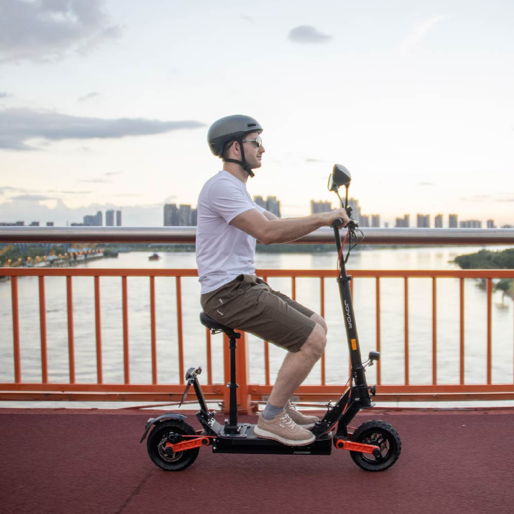 Uomo guida monopattino elettrico con sedile su ponte, skyline città sfondo.
