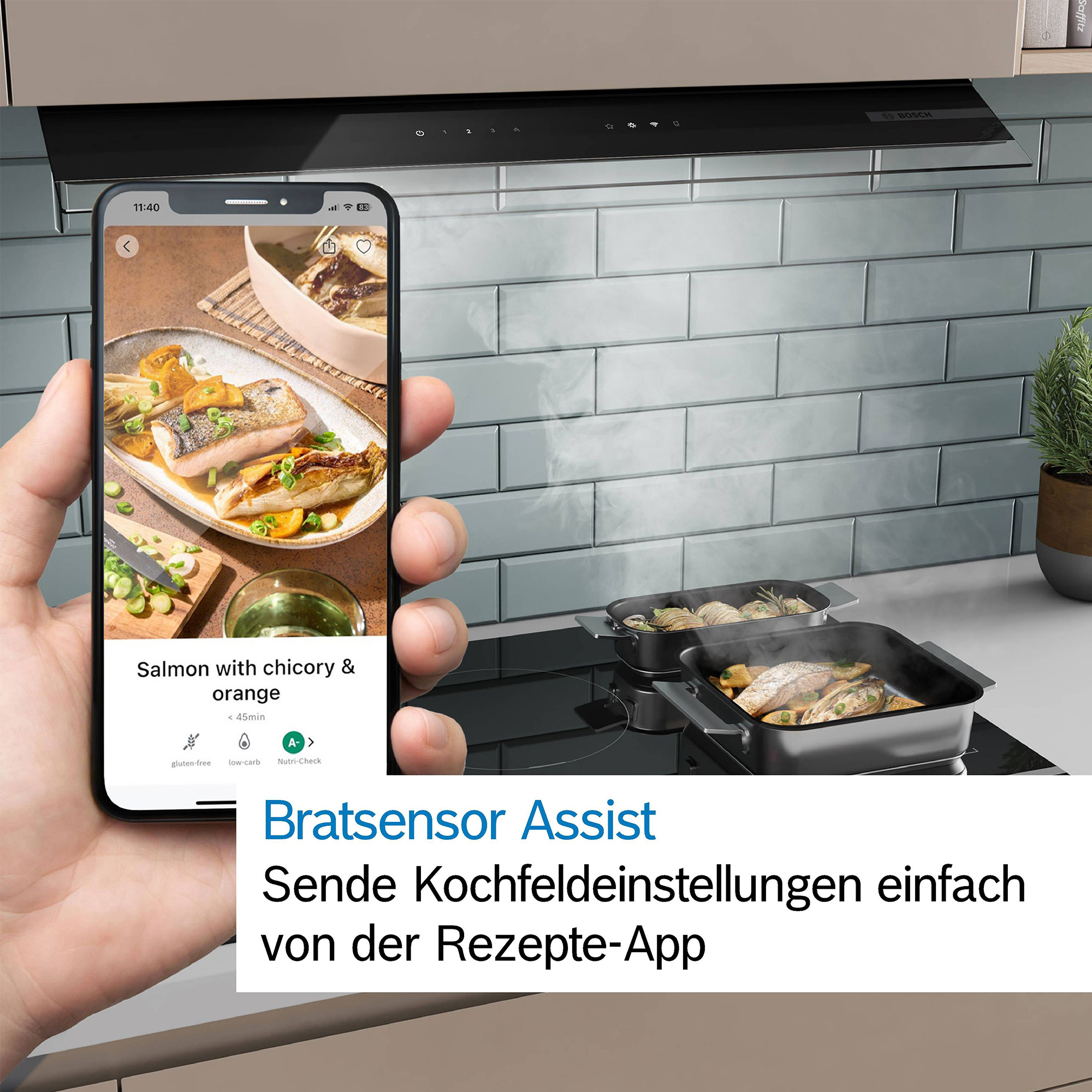 Eine Hand hält ein Smartphone mit einem Rezept für Lachs vor einem Kochfeld mit zwei Bratpfannen.