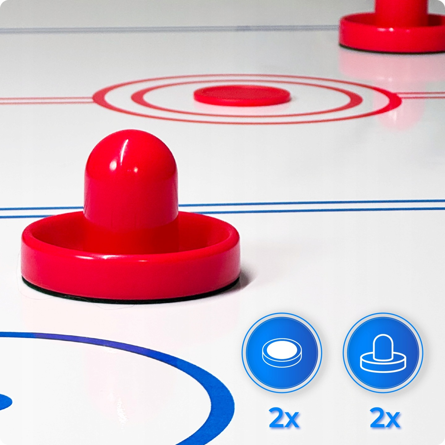 Dwa czerwone krążki i dwie czerwone łopatki na stole do air hockeya.