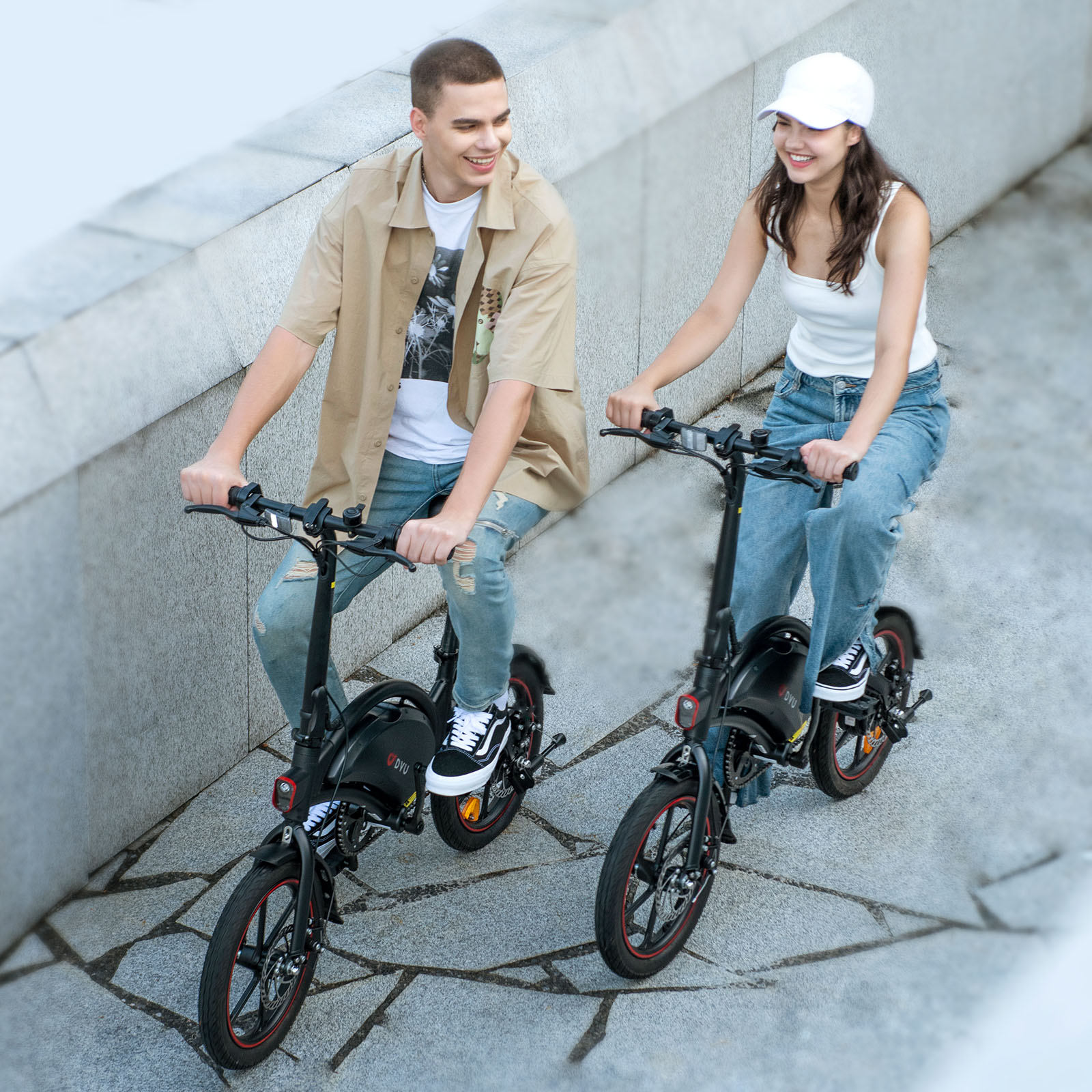 Un hombre y una mujer montan e-bikes negras una al lado de la otra en una superficie pavimentada.