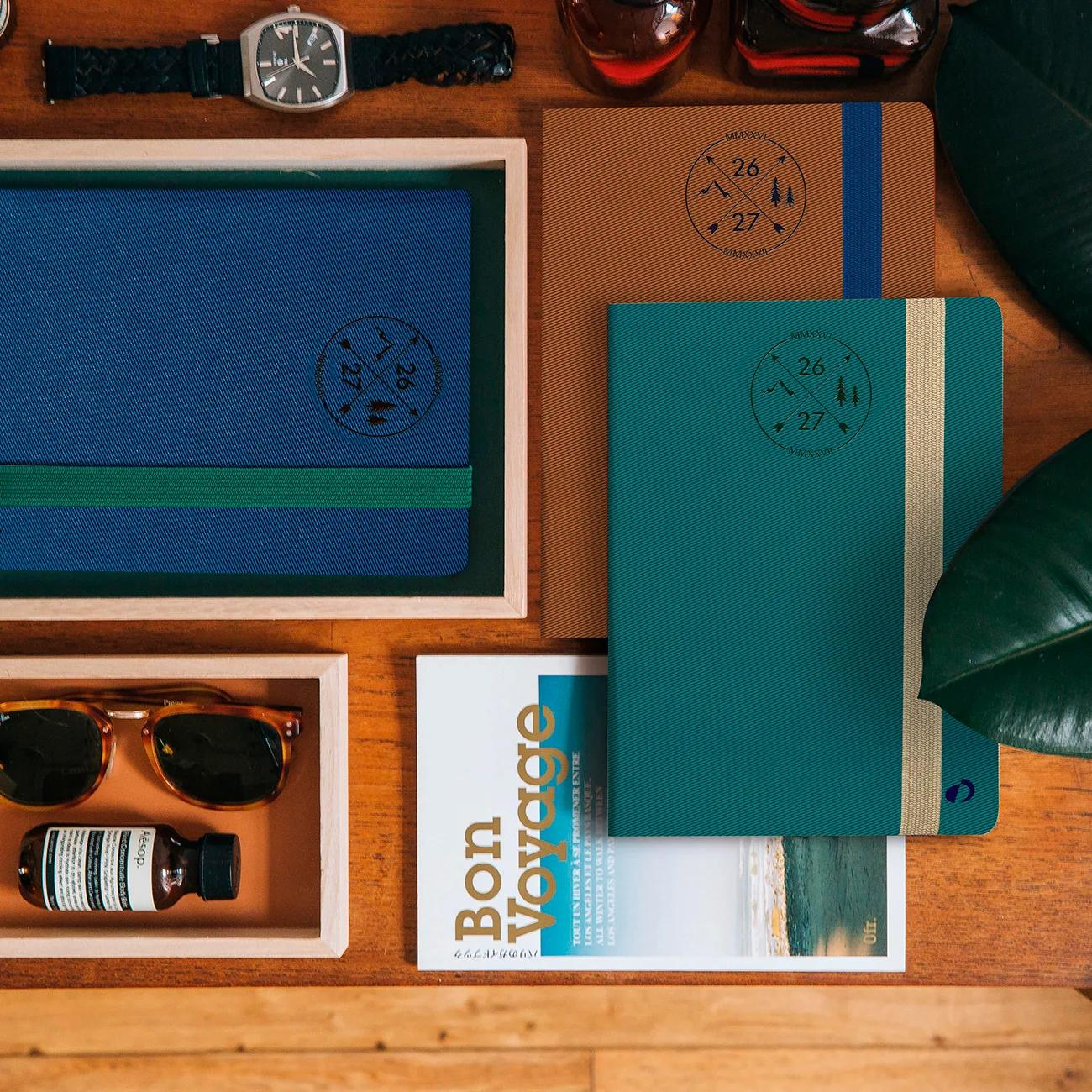 Una mesa con cuadernos, gafas de sol, perfume y un libro.