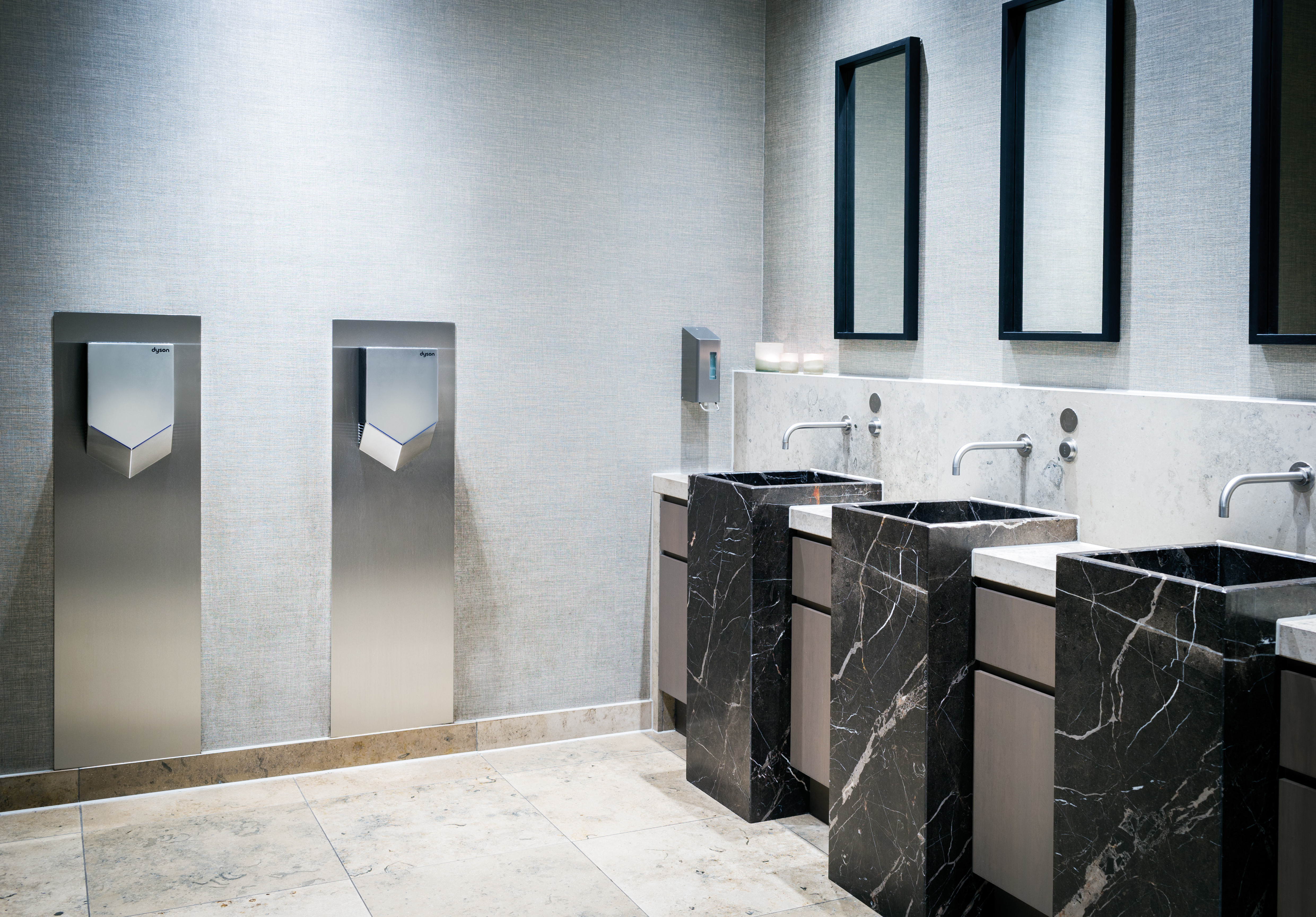 Bagno moderno con tre lavandini in marmo, specchi e asciugamani Dyson.