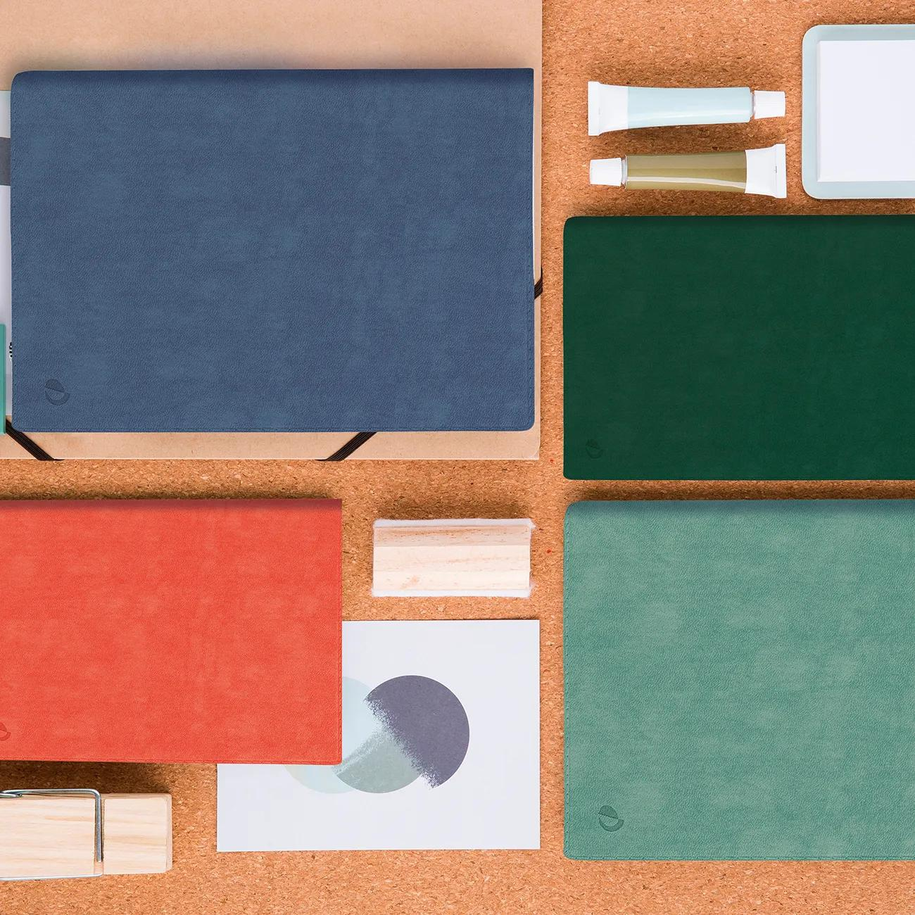 Vista superior de papelería: cuadernos azul, rojo, verde, turquesa, tubos, tarjetas y bloques madera.
