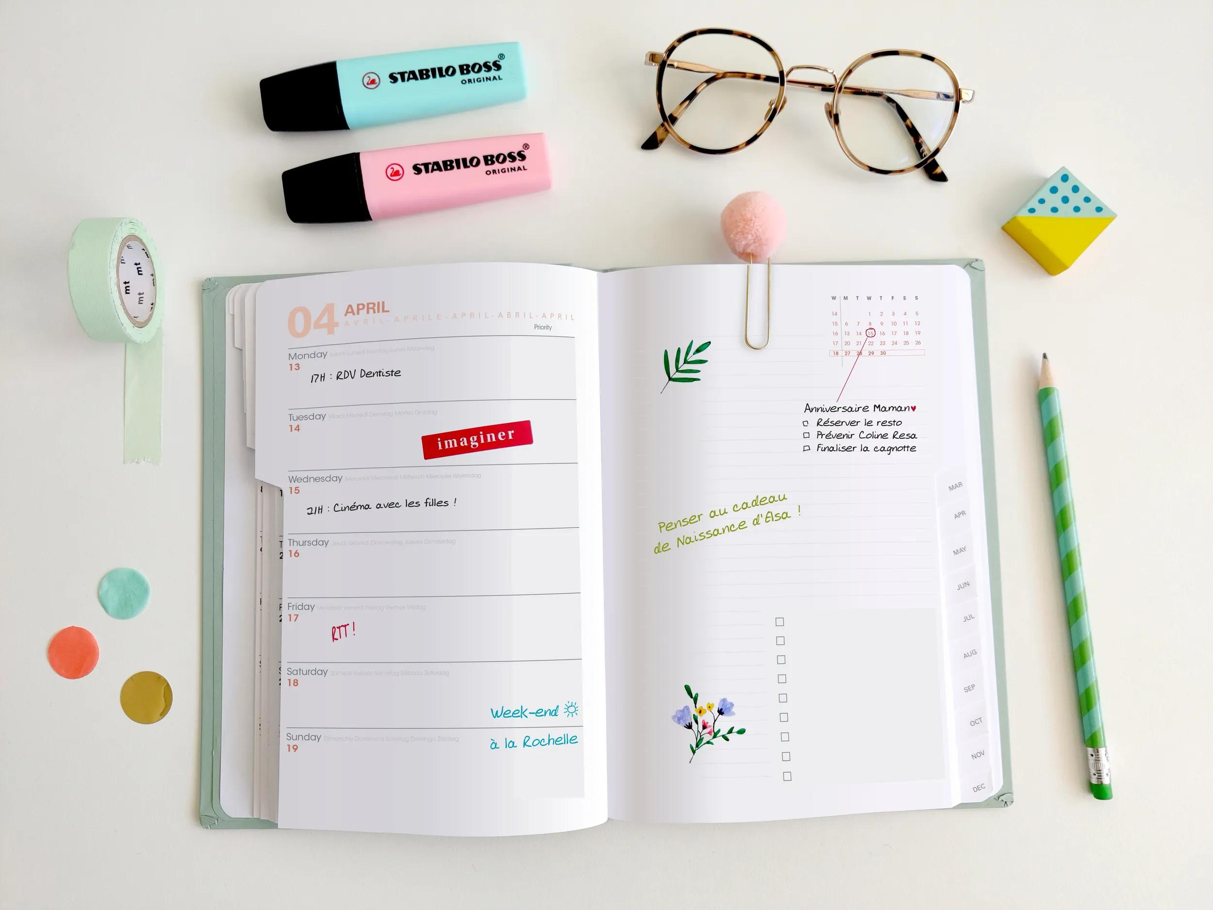Un escritorio con agenda abierta, bolígrafos, marcadores, gafas y cinta.