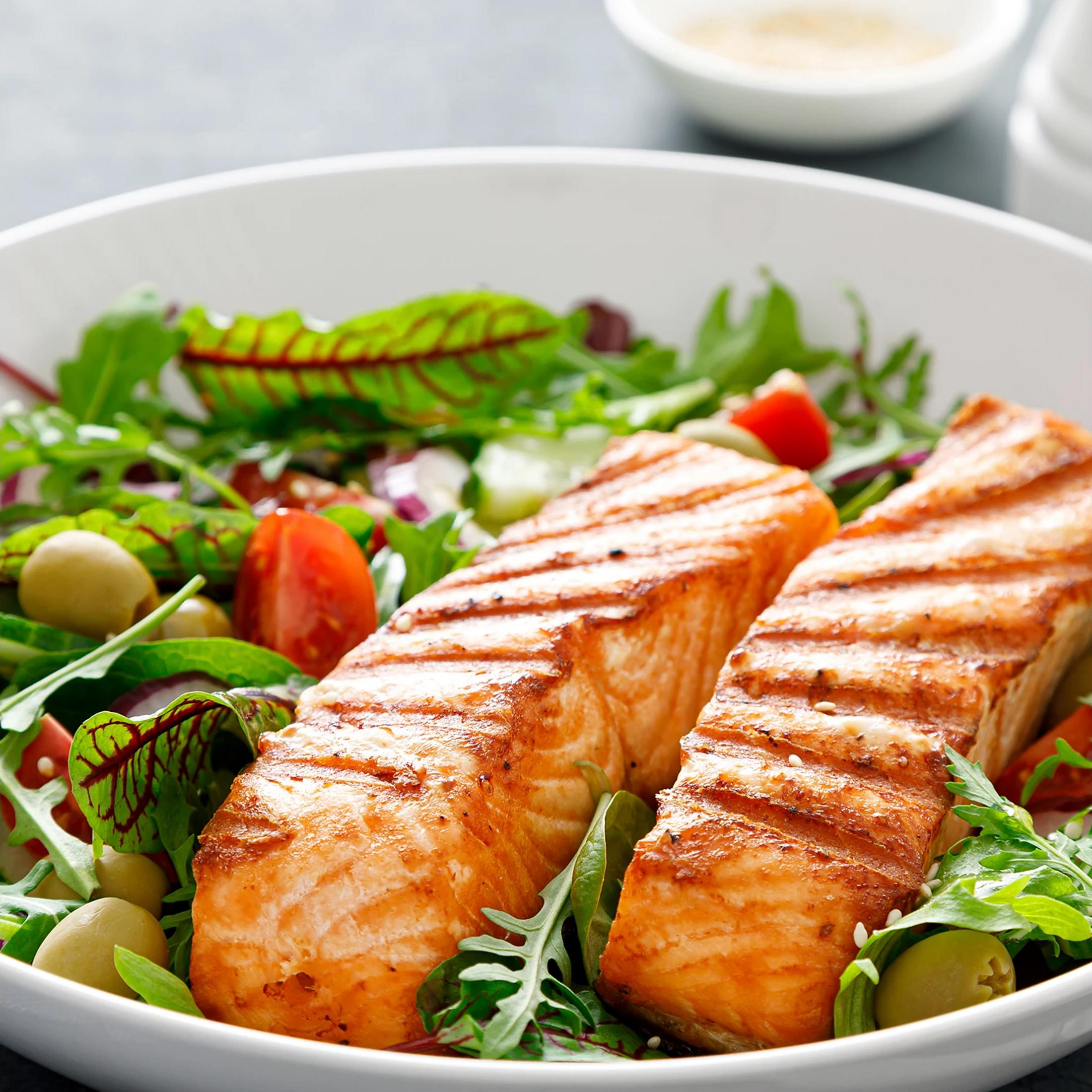 Due tranci di salmone grigliato su un'insalata con pomodori e olive.