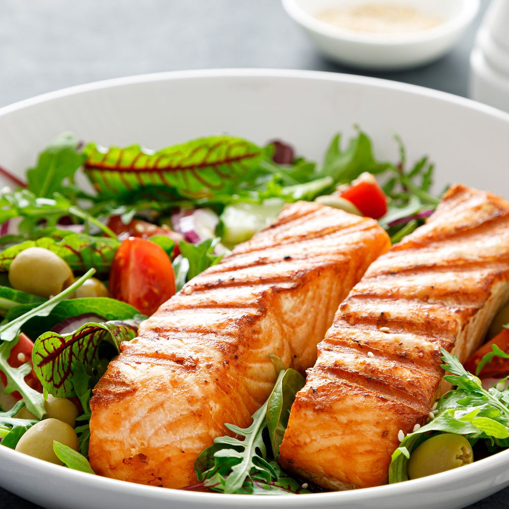 Due filetti di salmone grigliato su un'insalata con pomodori e olive.